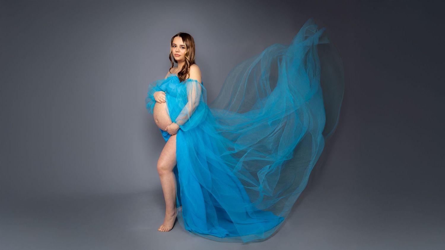 Ethereal portrait featuring a flowing turquoise blue dress against a dark gray backdrop. maternity photo, pregnancy photo