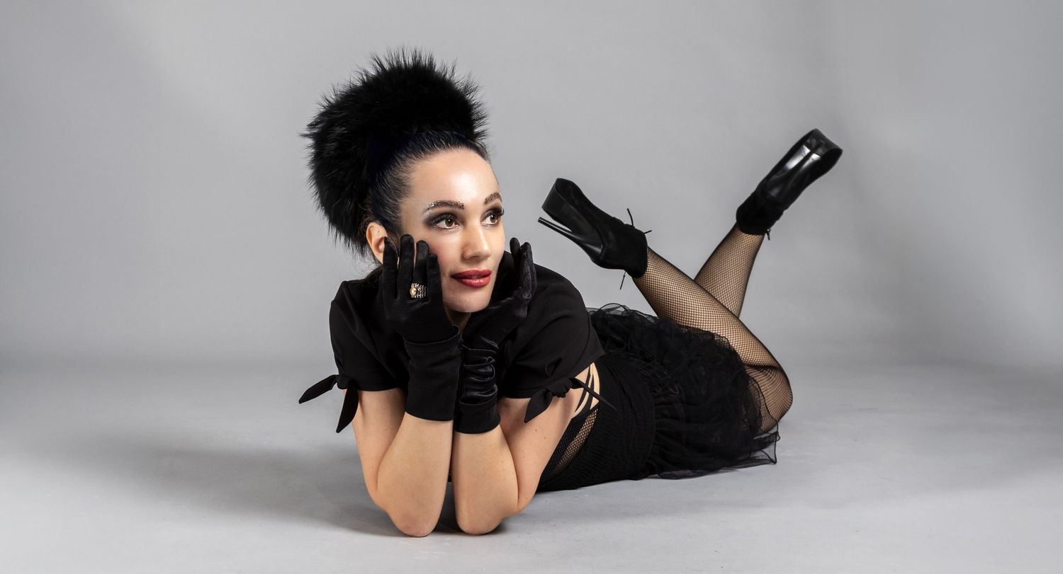 A girl in black clothes and feathered accessories poses dramatically on a light gray studio floor. best fashion photographer in Newport.