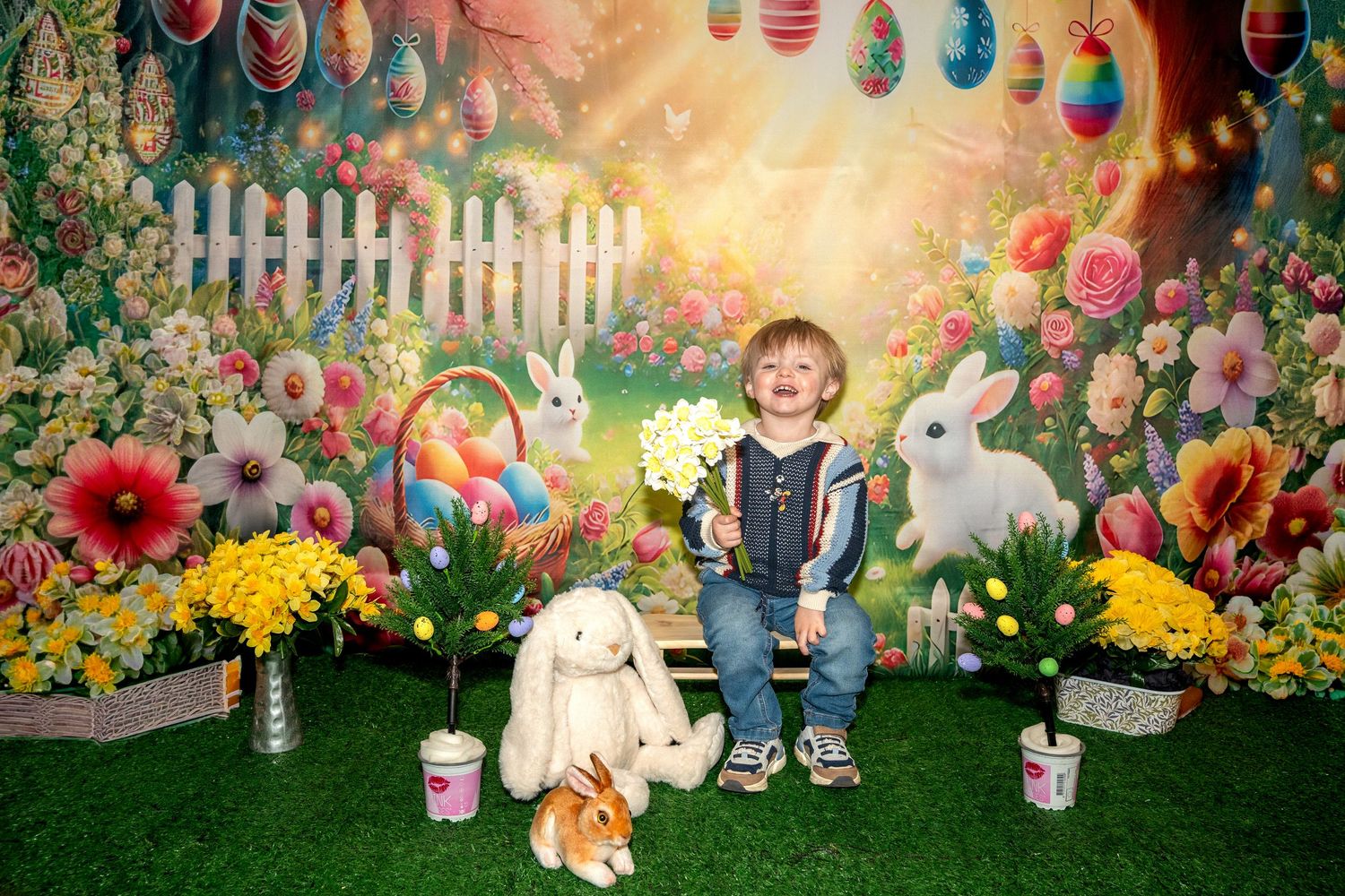 Colorful Easter scene with spring flowers, decorative eggs, white bunnies, and festive decorations on artificial grass.