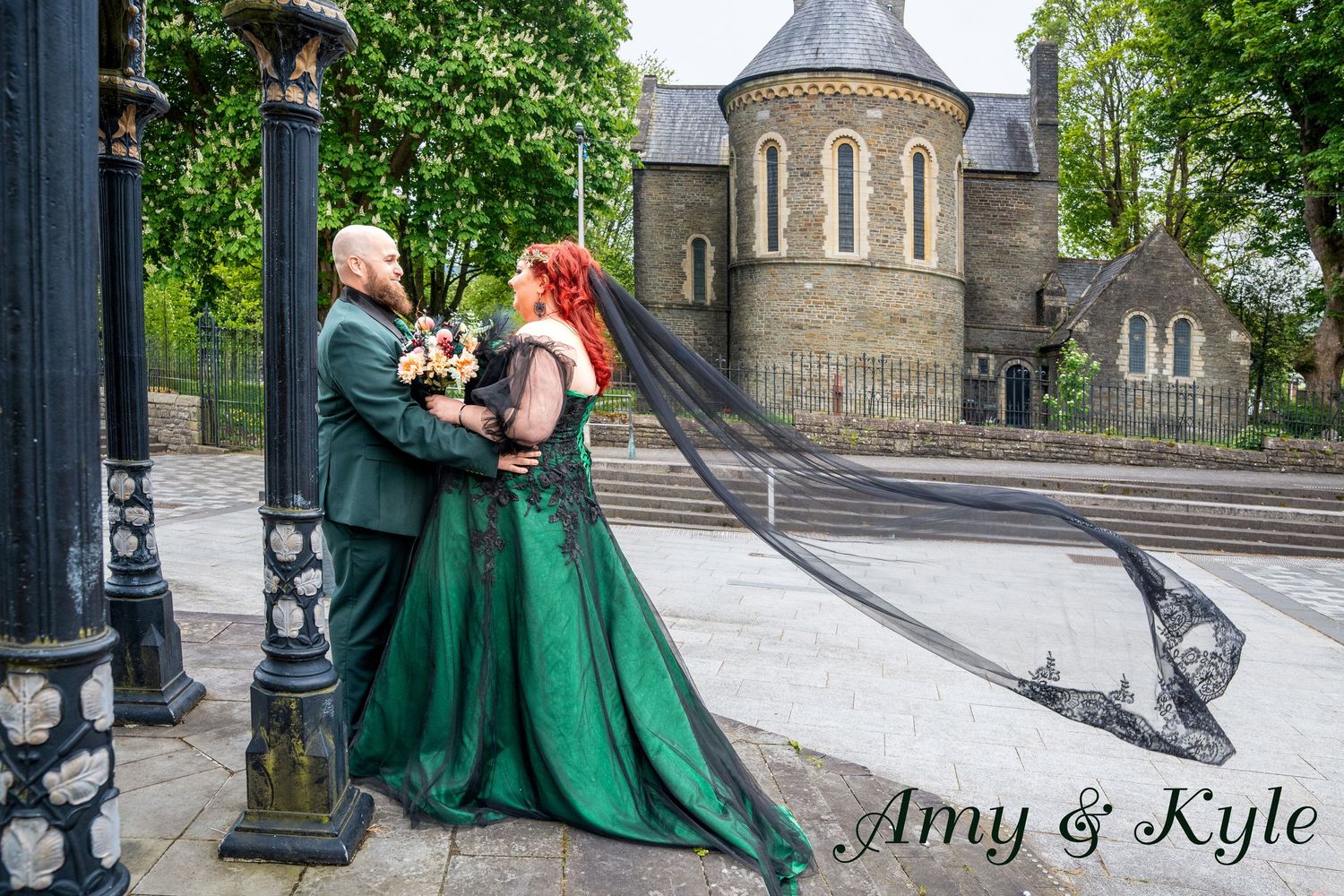 Amy and Kyle share a romantic embrace in wedding attire, bride in emerald gown with black veil, groom in green suit.