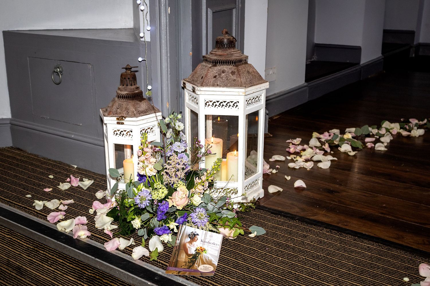 Decorative white lanterns with rustic tops surrounded by scattered flower petals on dark wooden floor.