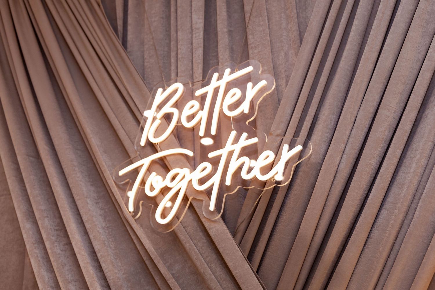 Neon white 'Better Together' text sign glows against brown palm leaf background.