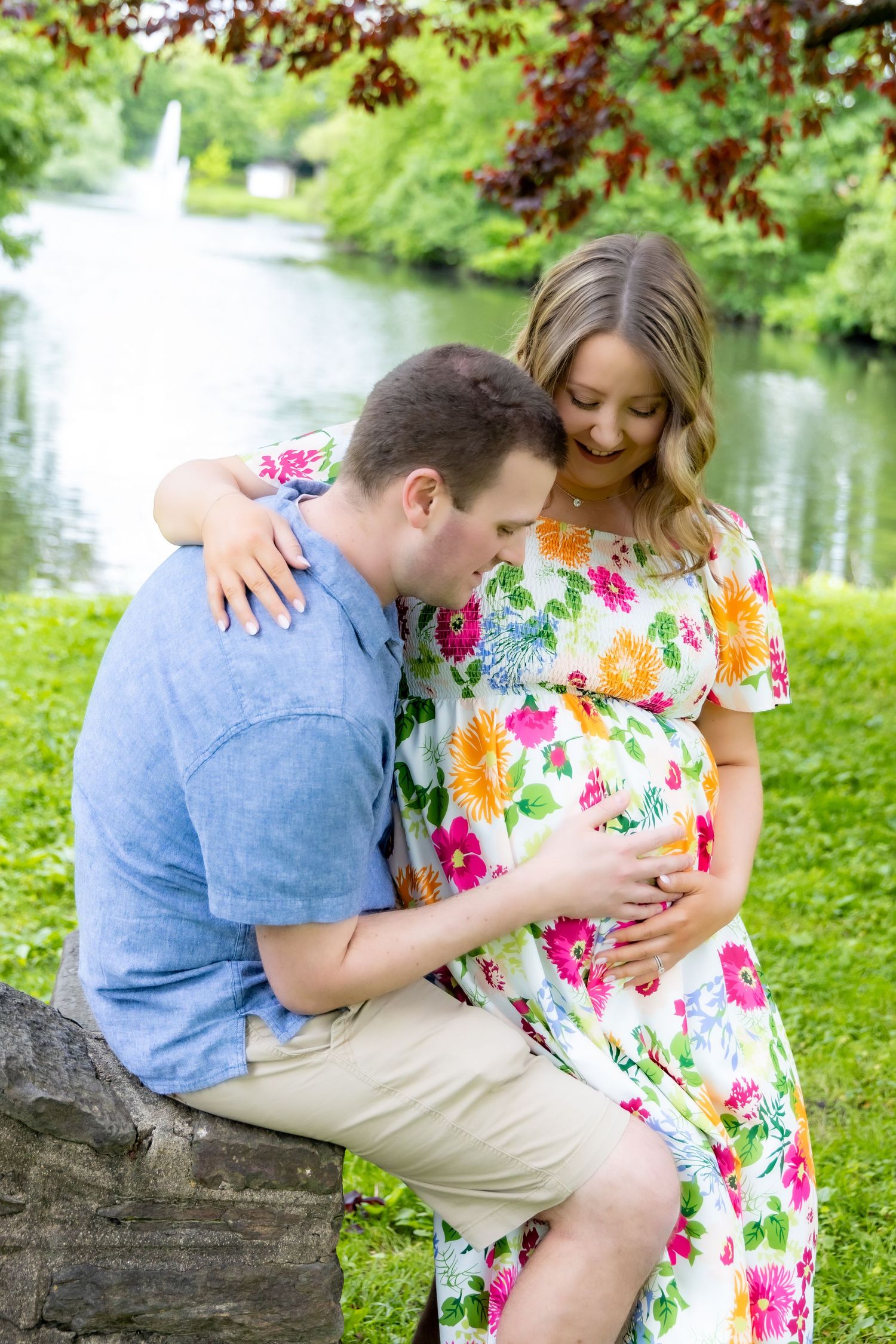 A romantic moment captured by a lake with a colorful floral dress against a lush green background and fountain.