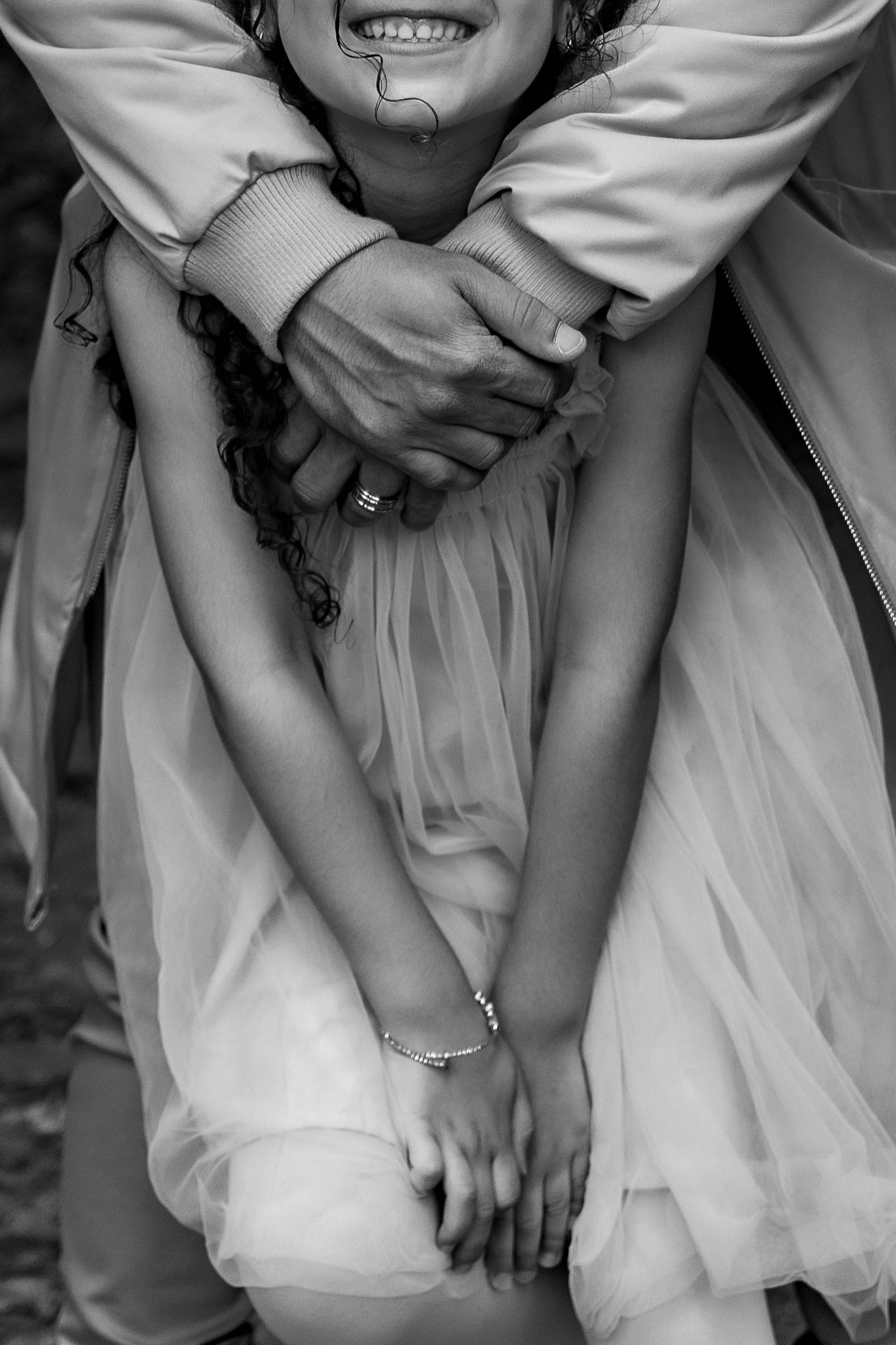 Black and white close-up of hands clasped together while wearing a flowy white dress and showing rings.