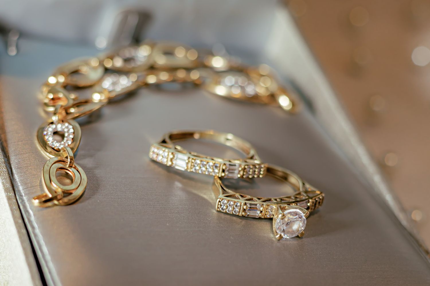 Close-up photograph of elegant gold diamond jewelry including a bracelet and rings on a reflective surface.