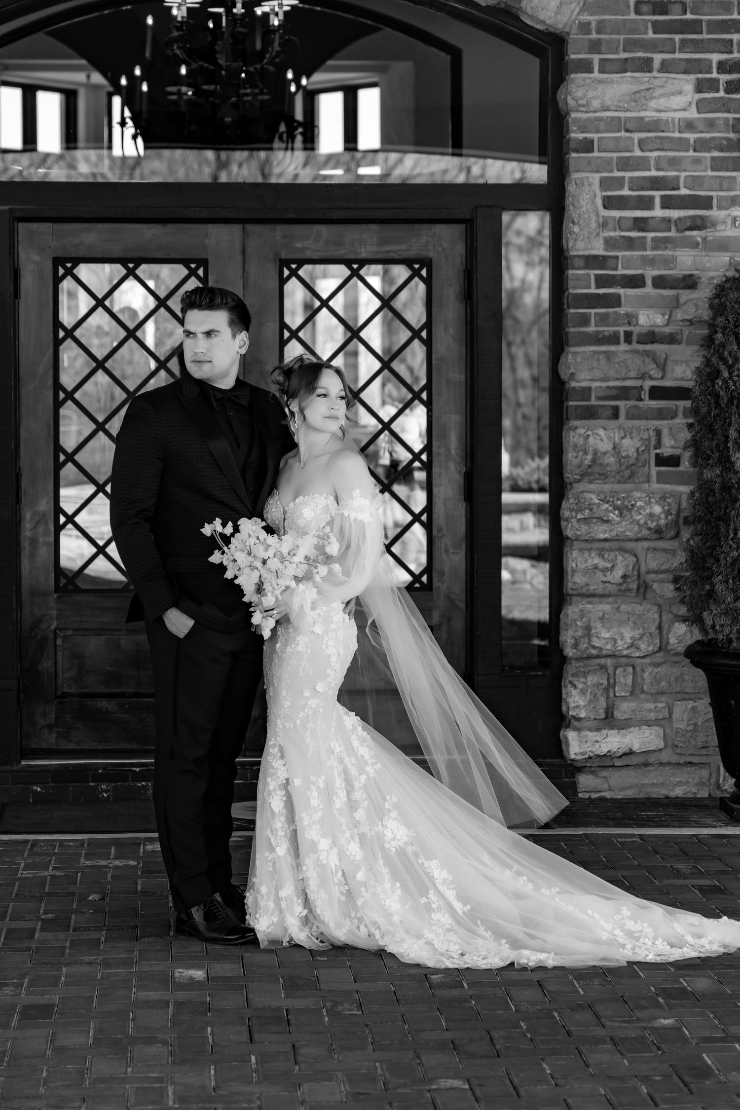 Classic black and white wedding portrait in front of stone archway with diamond windows.