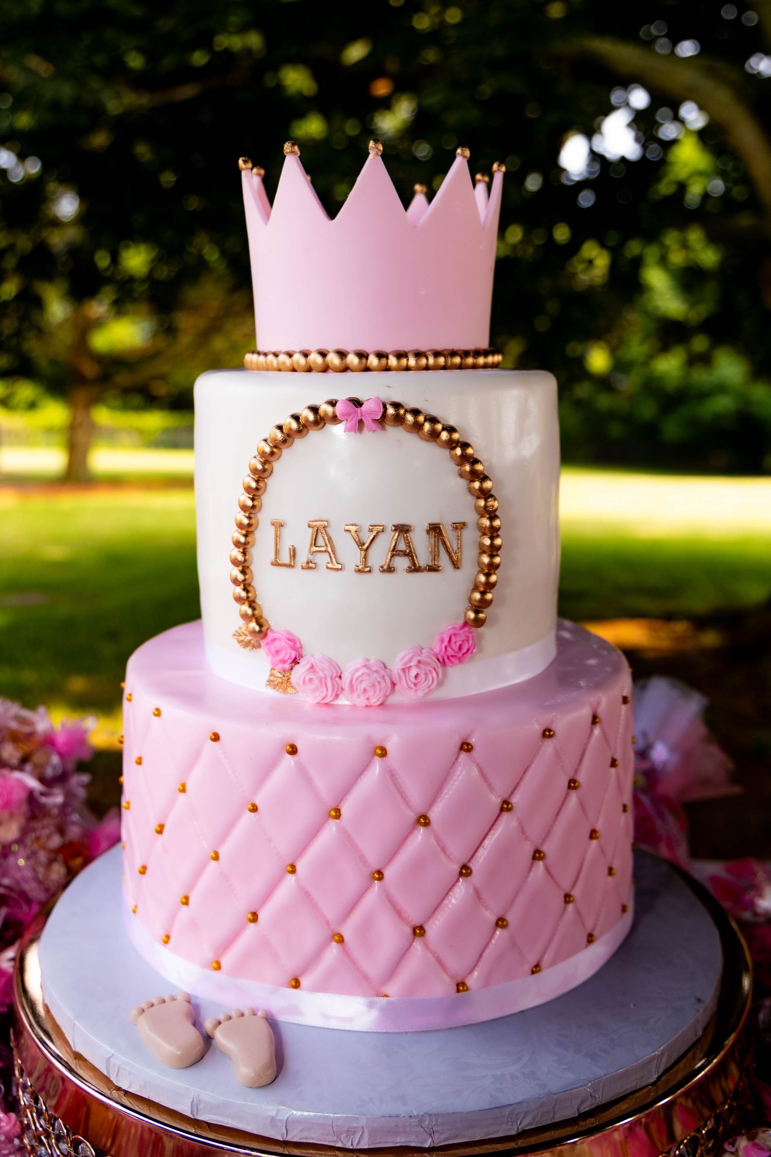 Elegant pink and white princess cake with crown topper and 'LAYAN' name in gold details.
