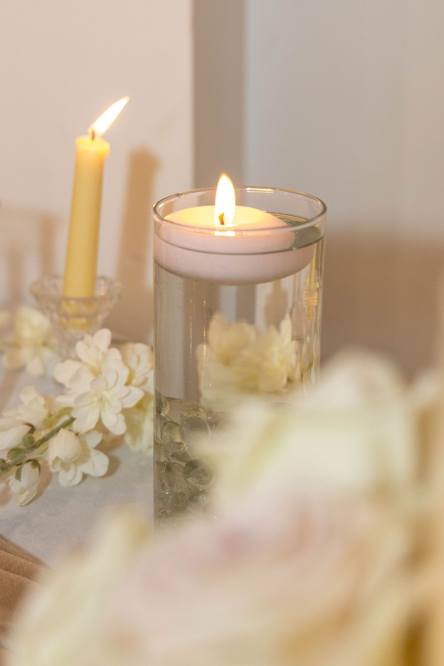 Glowing candles and delicate white flowers create a serene and romantic atmosphere in soft lighting.