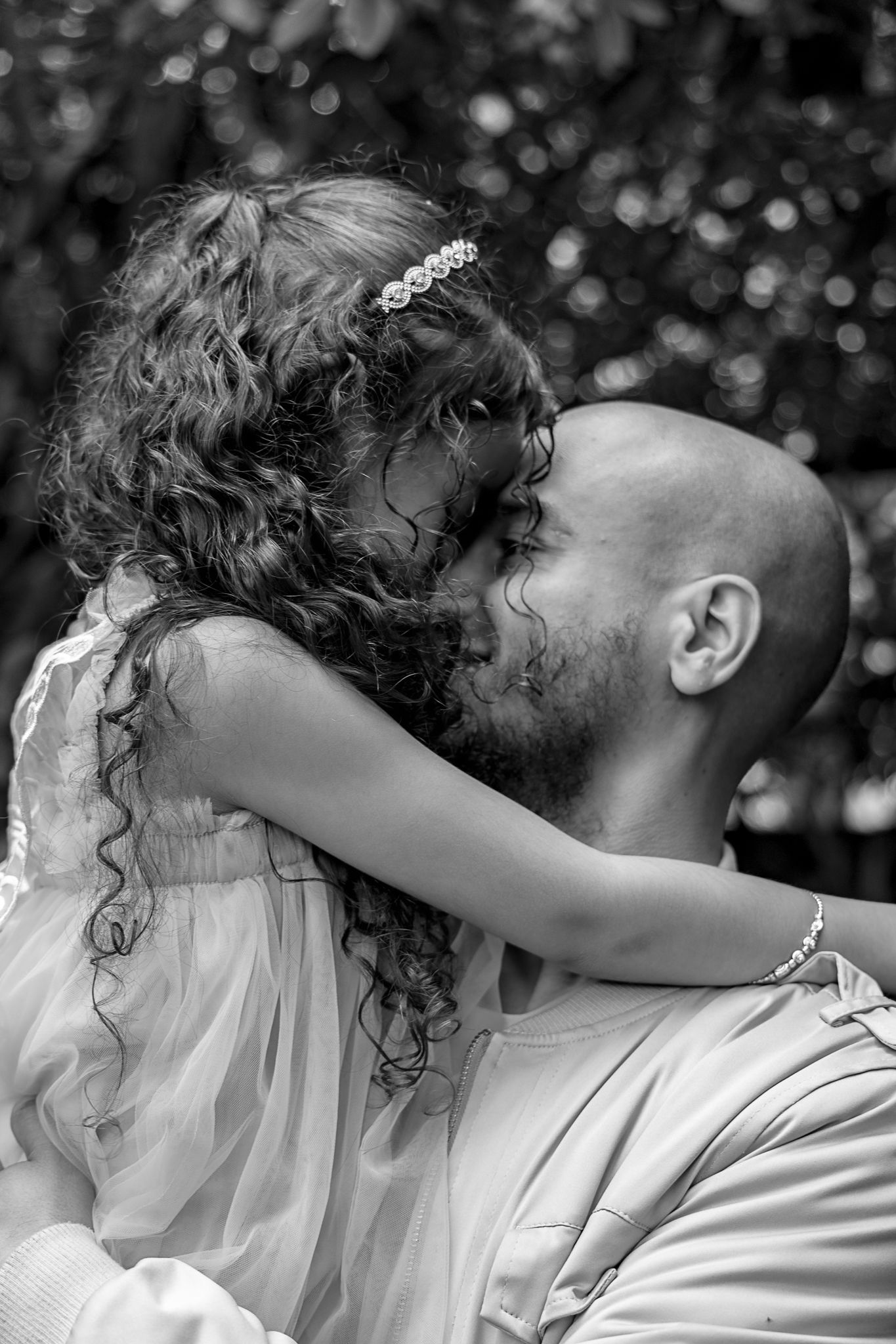 A tender black and white photo showing a father and daughter sharing an affectionate moment outdoors.