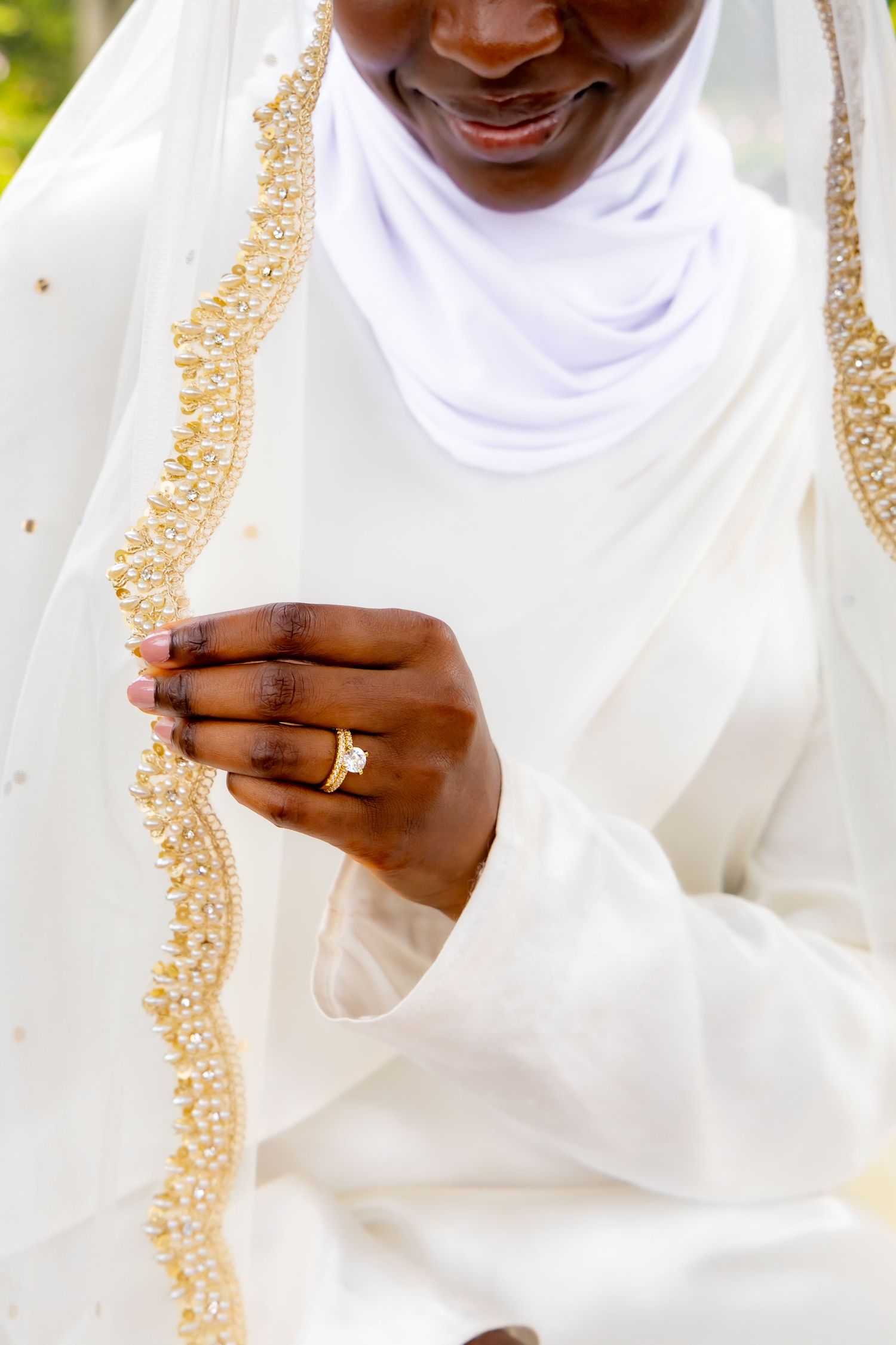 Close-up of hands showing engagement ring against white and gold embellished traditional wedding attire. | PHL, PA Wedding Photographer