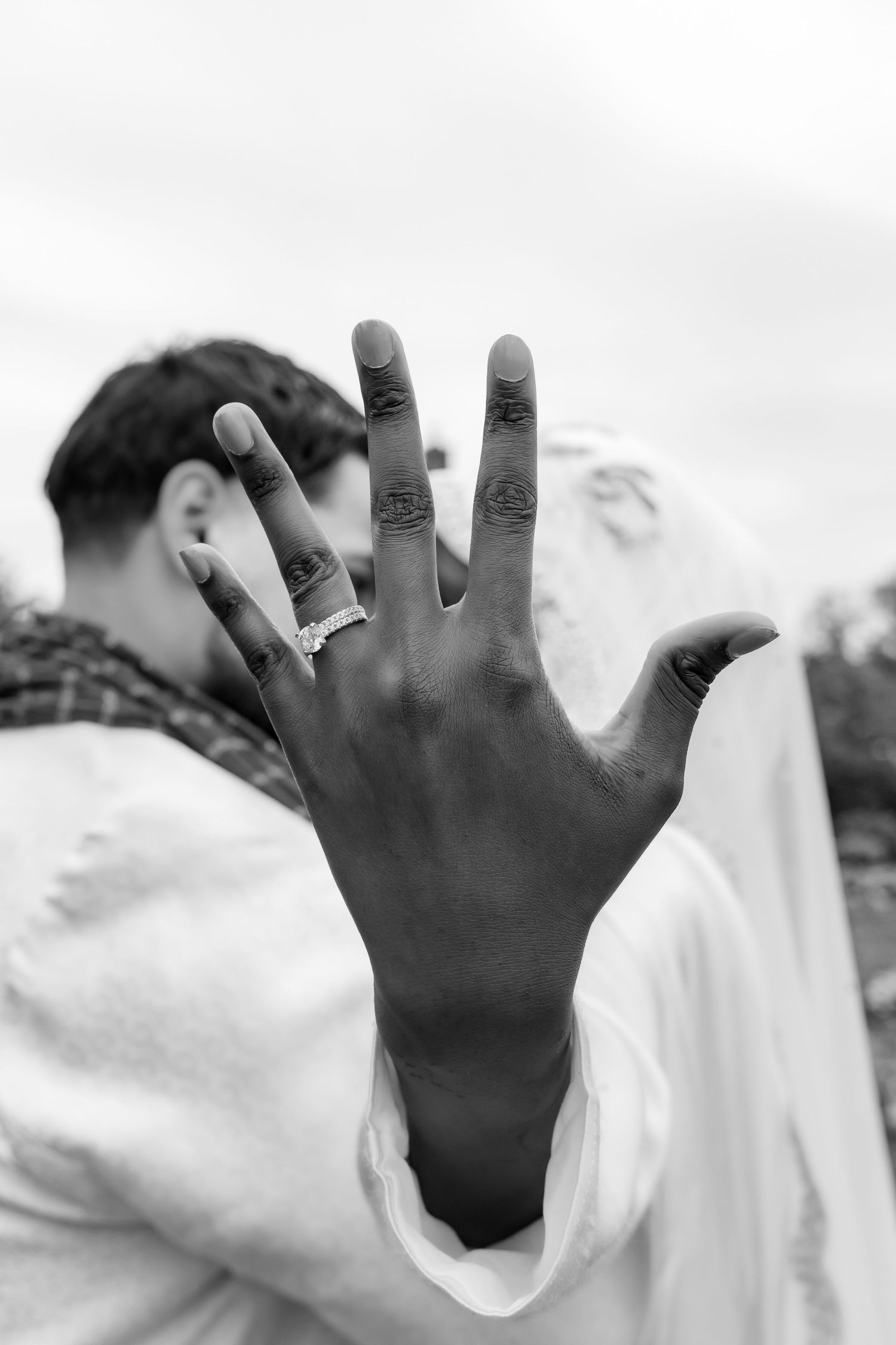 A black and white photo showing a hand with a wedding ring held up against a bright sky. | PHL, PA Wedding Photographer | Desi Wedding