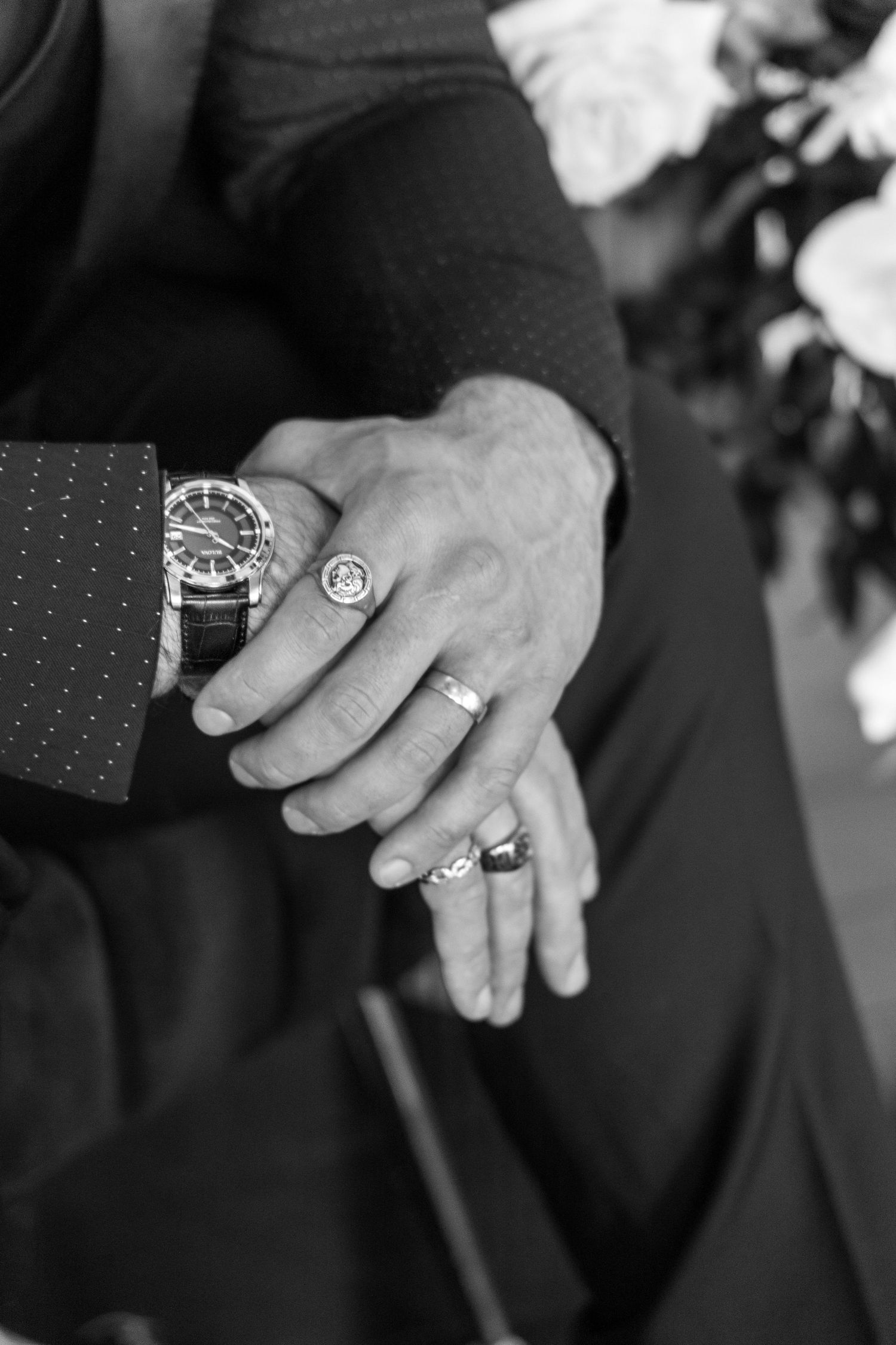 Black and white detail shot of hands showing wedding rings and luxury watch.