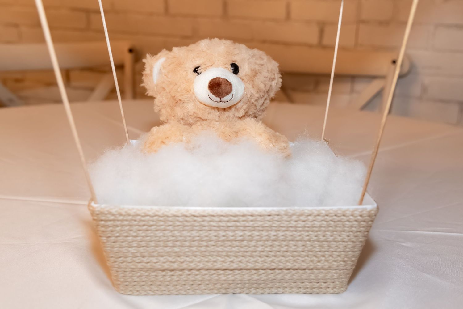 A cute teddy bear sits in a rope basket filled with fluffy white bath bubbles.