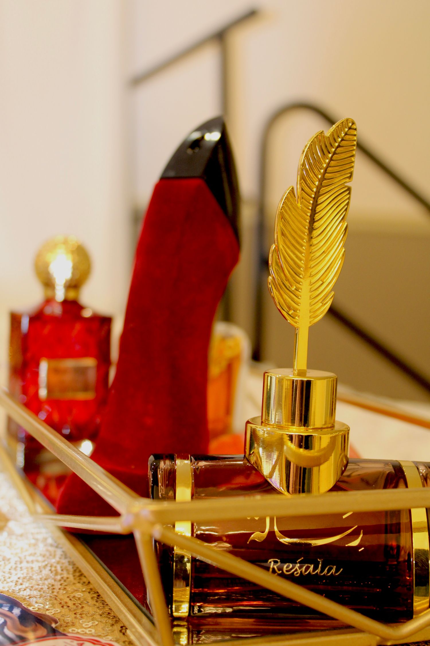 A luxurious perfume display featuring a red stiletto heel and a gold feather-topped bottle on an elegant mirrored surface.