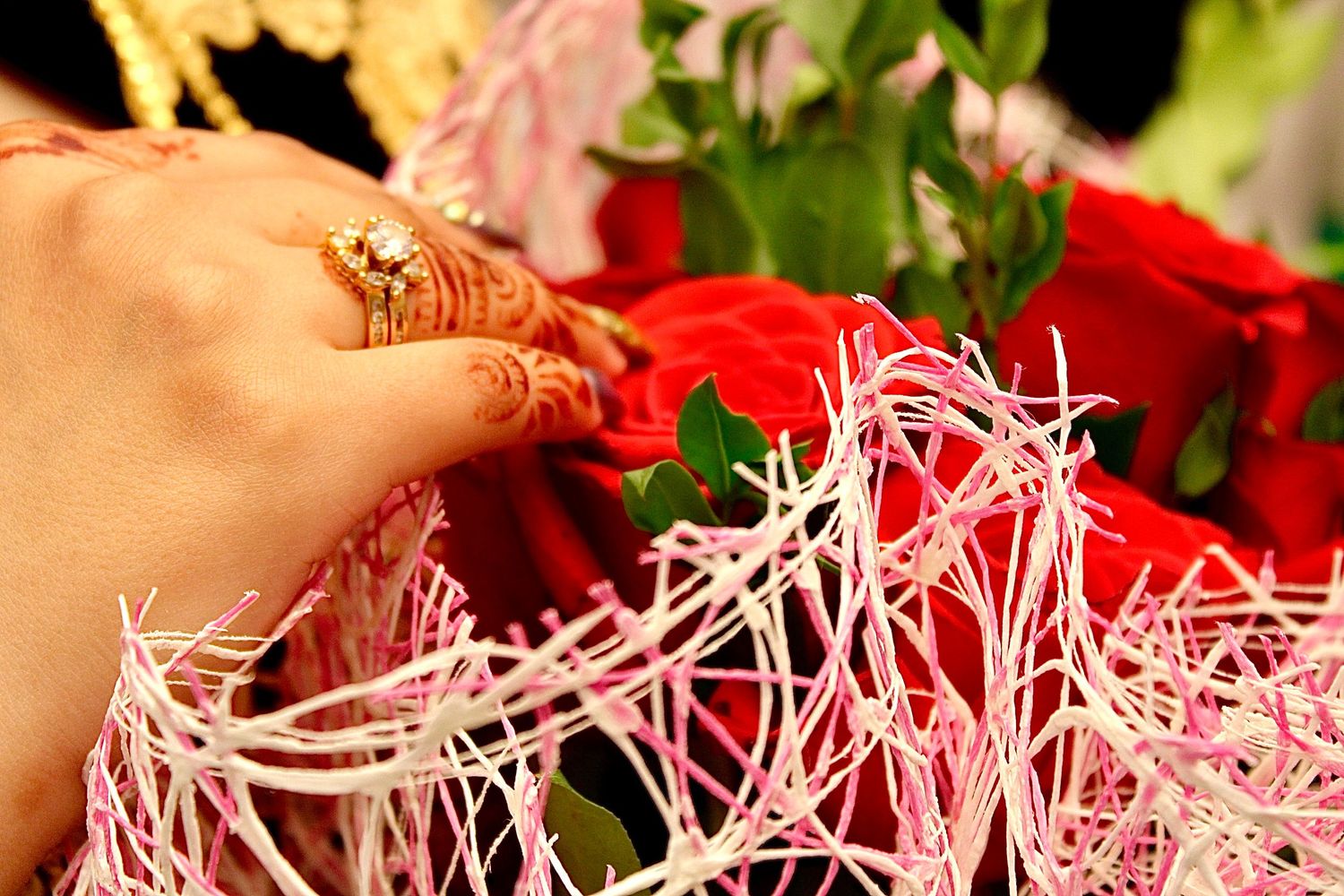 Hand with henna tattoo decorations arranging red roses with pink decorative fillers.