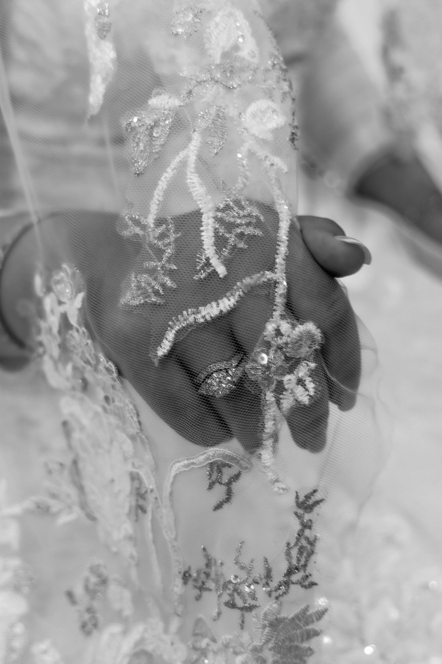 Black and white close-up of delicate lace details on fabric with intricate floral embroidery patterns.