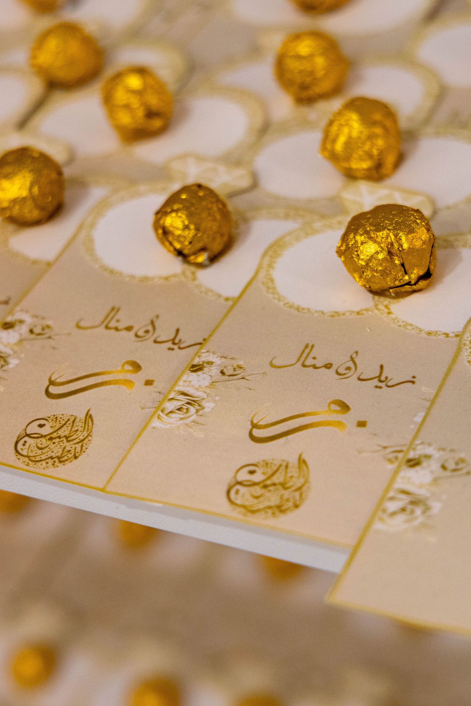 Elegant gold foil wrapped chocolates arranged on decorative cards with Arabic calligraphy designs.
