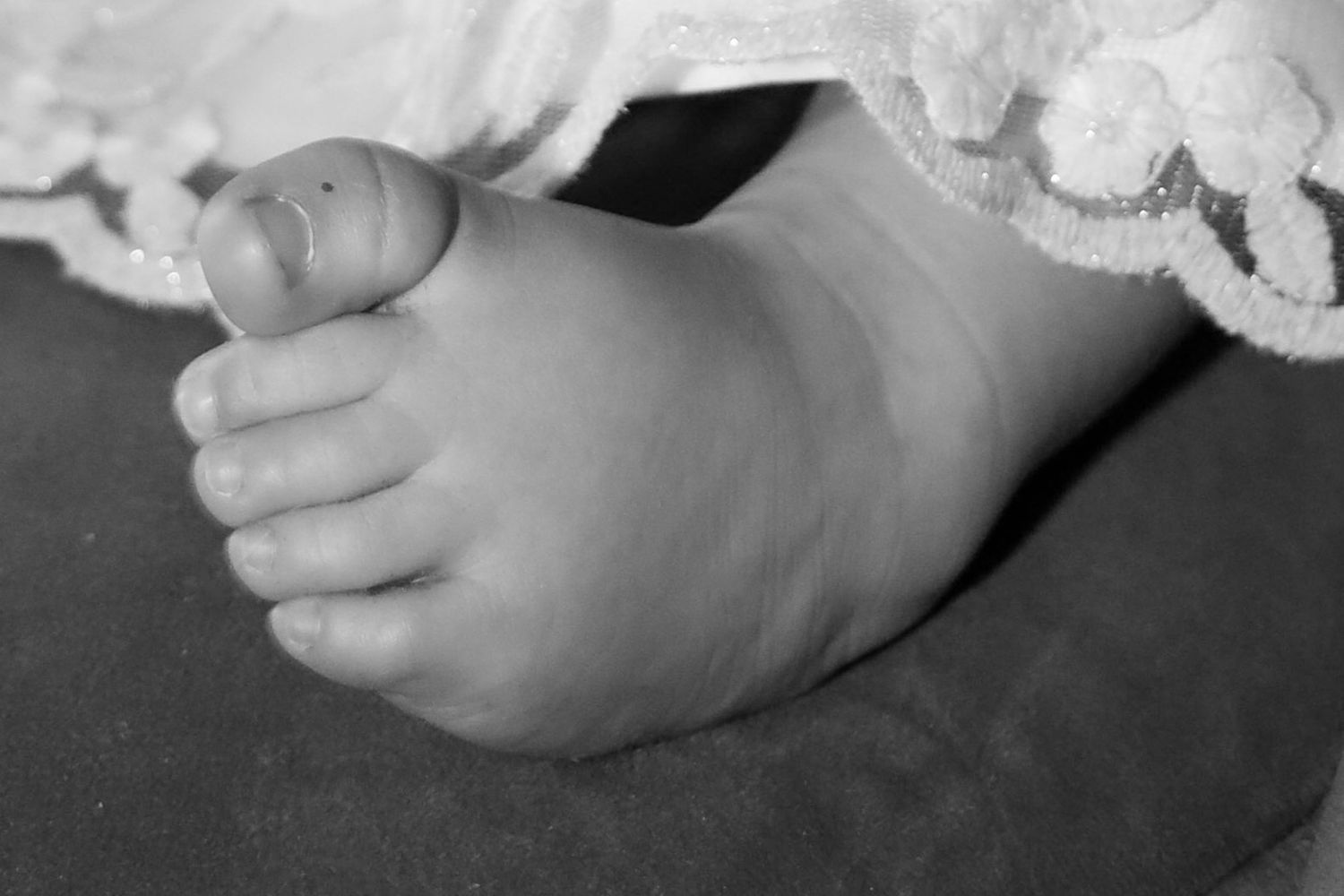 Close-up black and white photograph of a baby's tiny foot against a dark background.