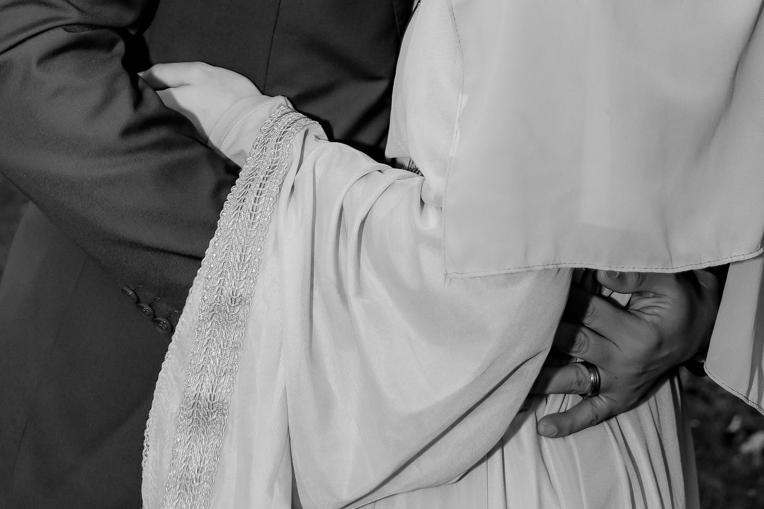 A close-up black and white photo showing hands holding white fabric in an intimate wedding ceremony moment.