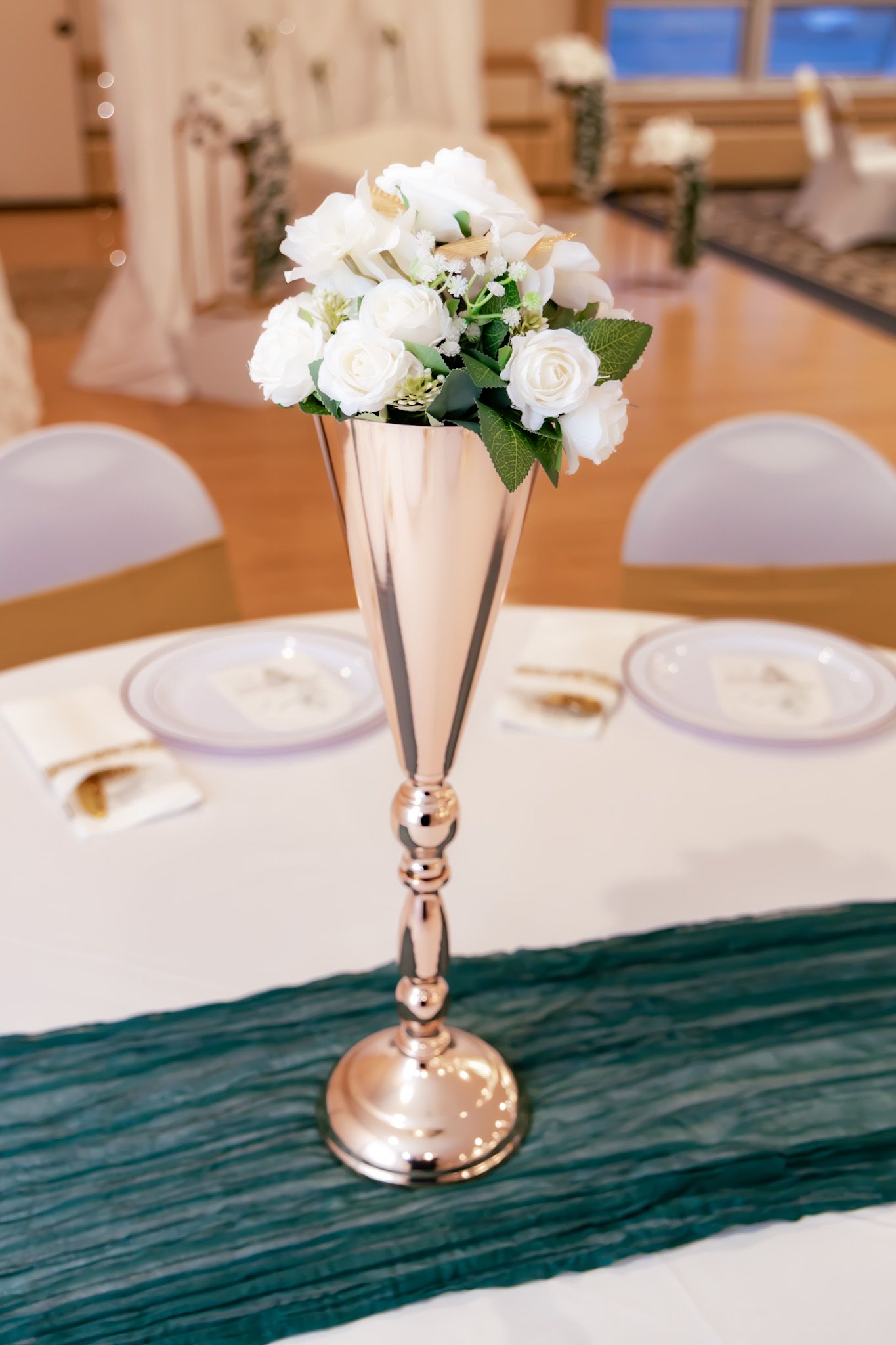Elegant silver trumpet vase with white roses centerpiece on a formal table setting.