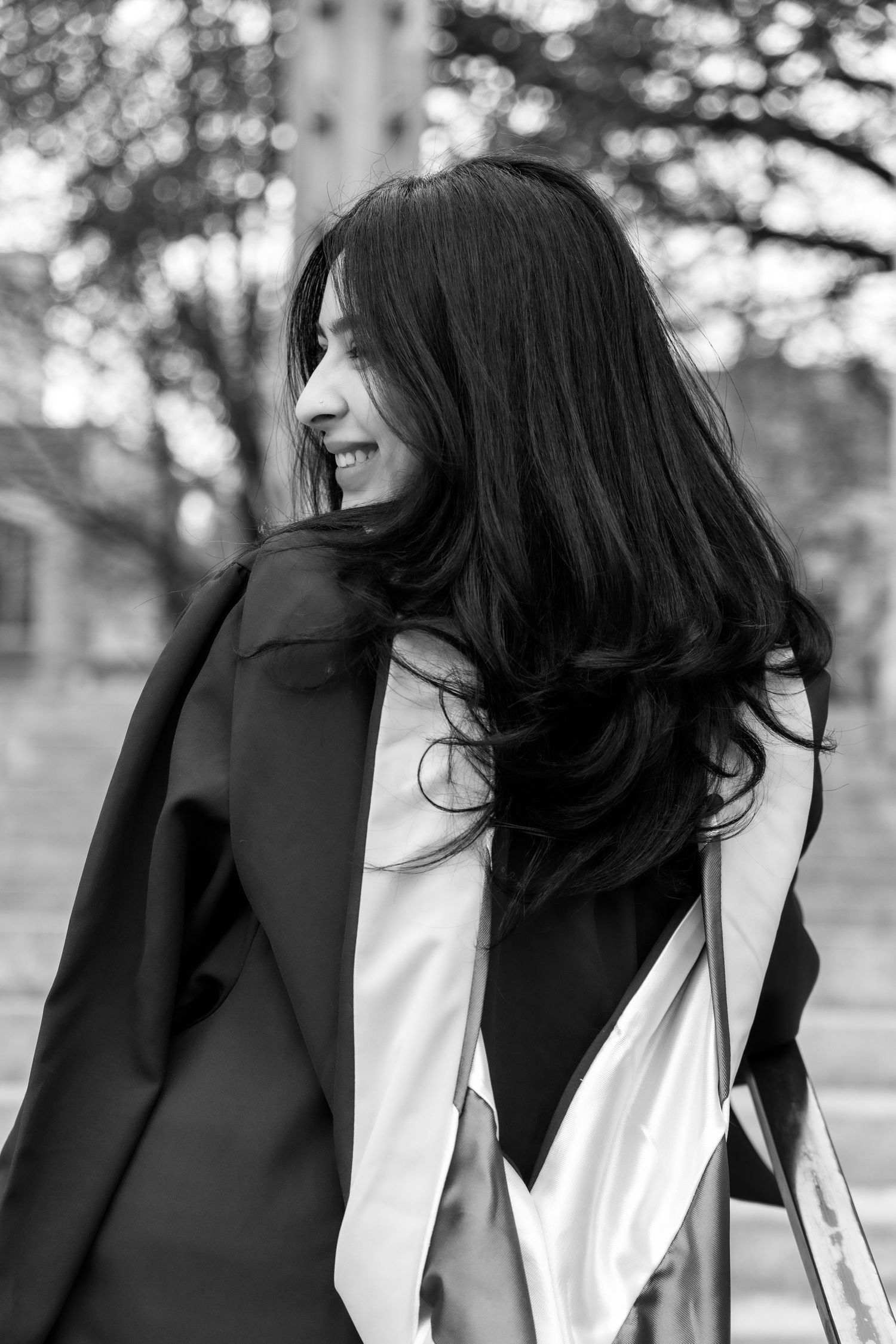 Black and white portrait of someone with long dark hair wearing a black coat and white top looking off to the side.