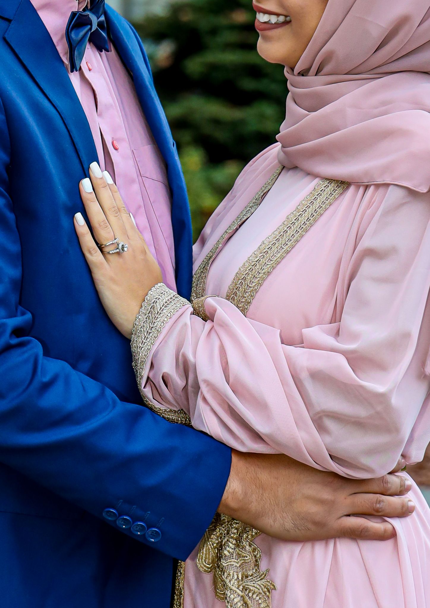 Close up of couple in formal attire with pink hijab and royal blue suit showing wedding ring and embellished details.