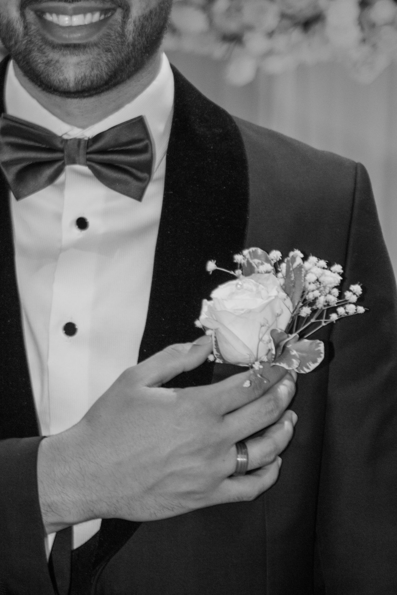 Classic black tuxedo with bow tie and white rose boutonniere in black and white photograph.