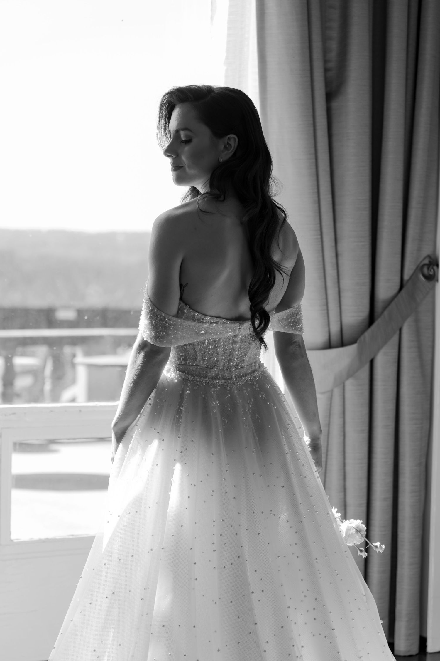 Silhouette of a wedding dress with sparkles against window light.