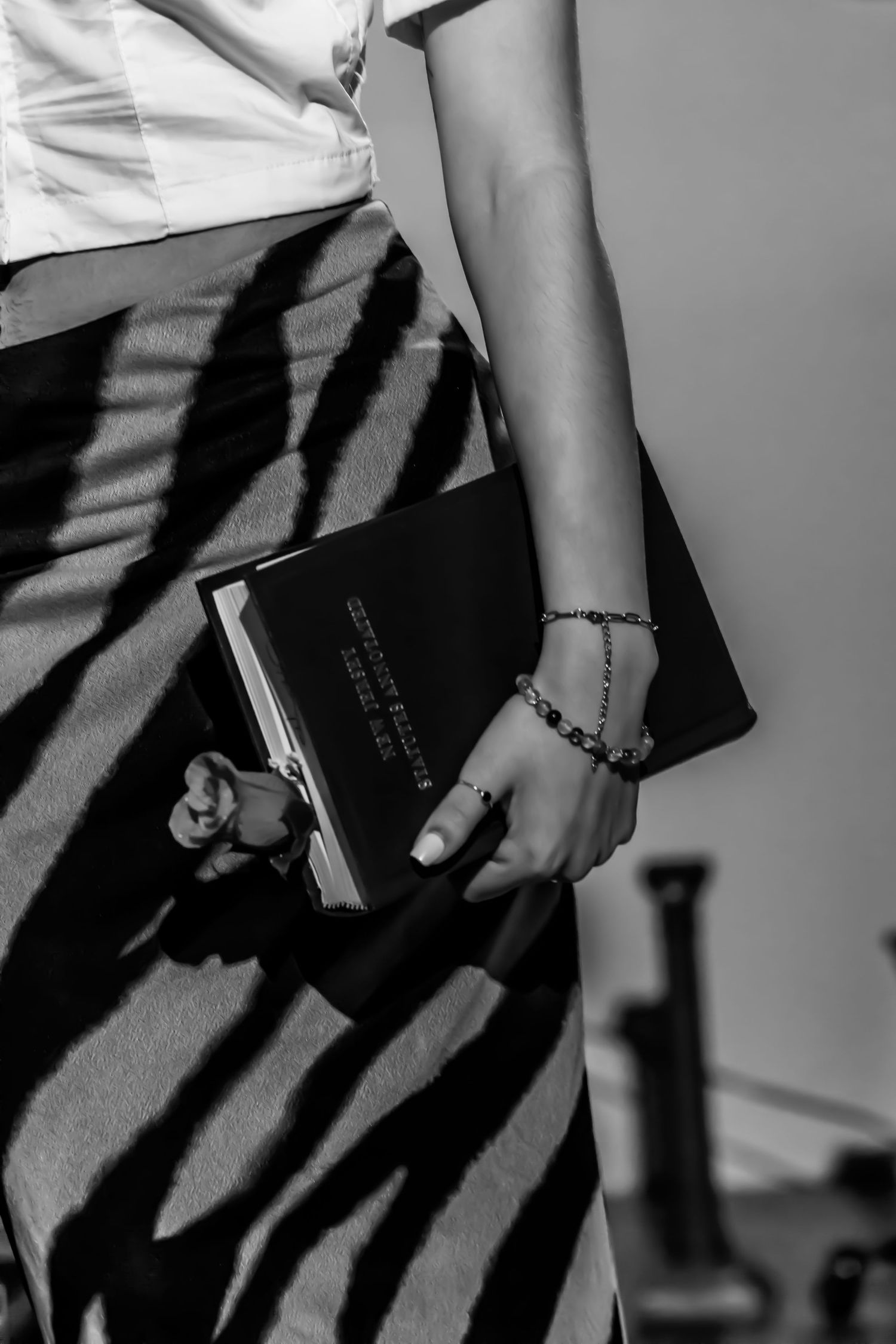 Black and white photo showing a hand wearing a bracelet holding a book with dramatic diagonal shadow lines.