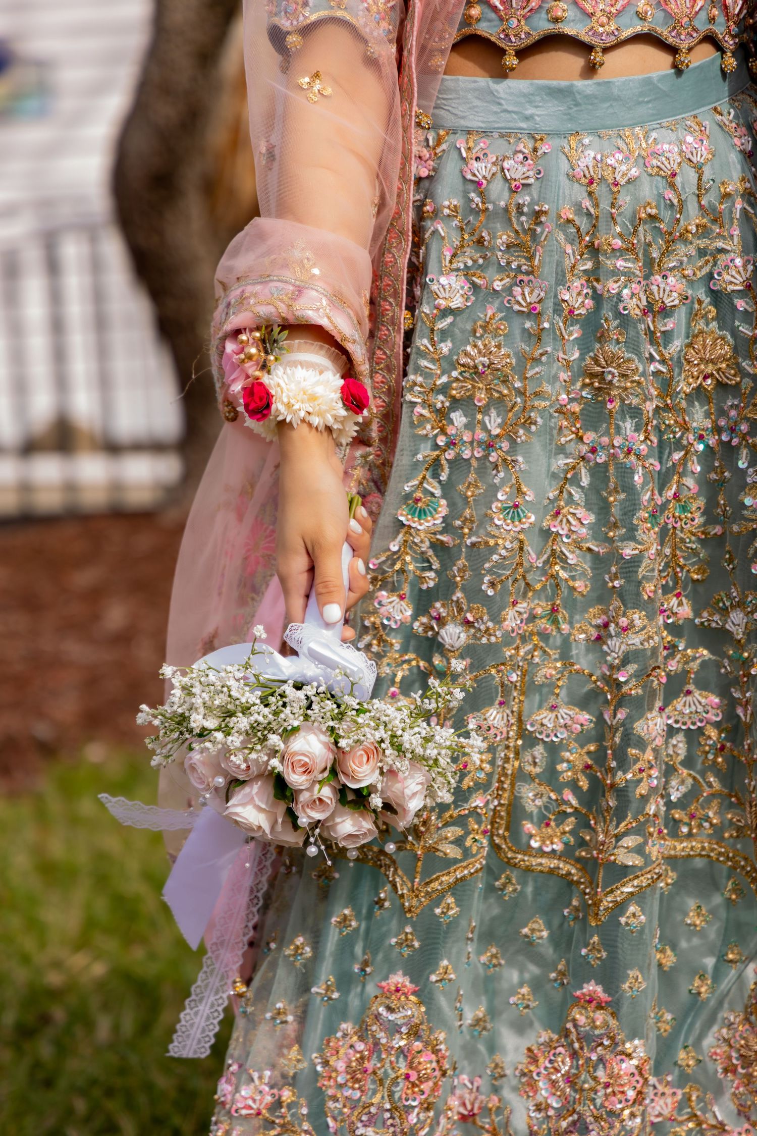 Close-up of traditional Indian bridal attire showing embellished teal lehenga and delicate floral bouquet.