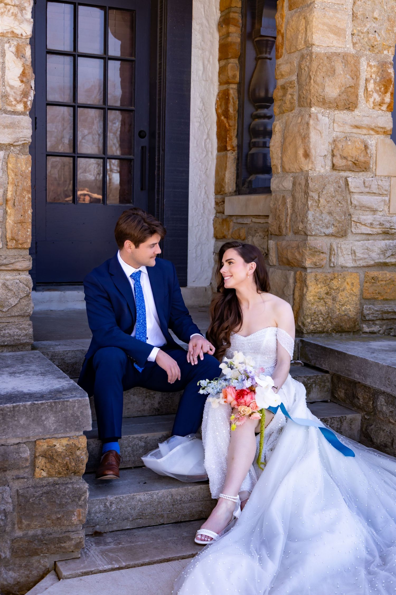 Romantic wedding couple sitting on stone steps of historic building.