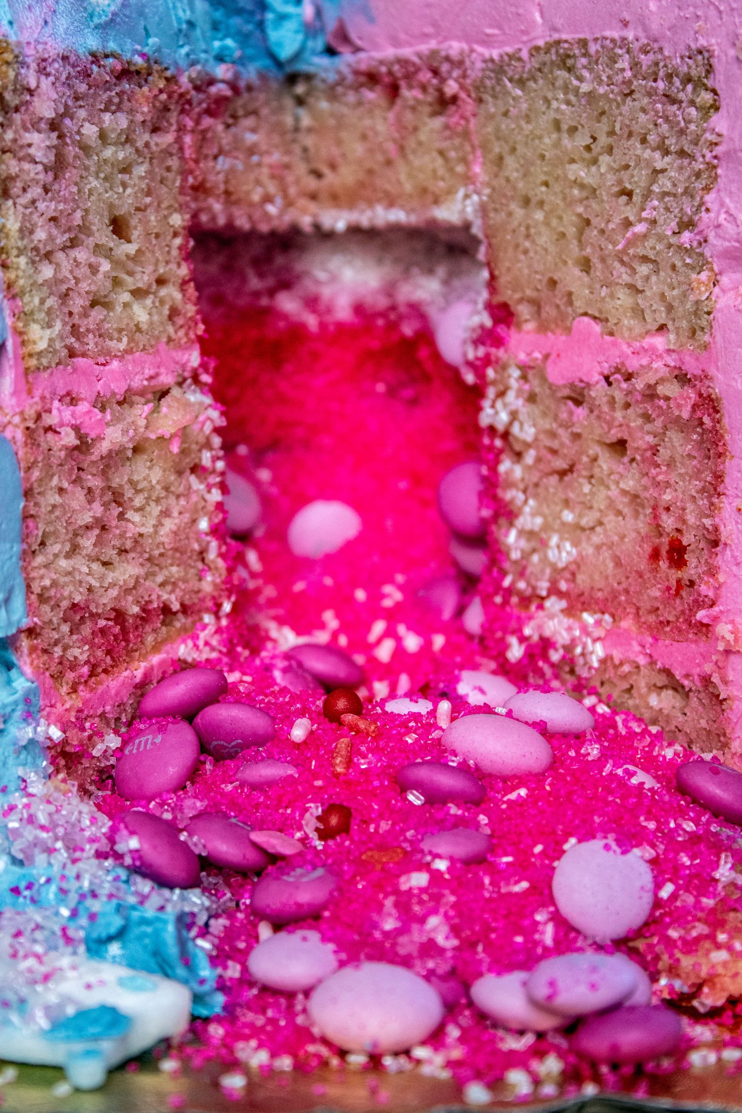 Close up of pink frosted cake with colorful candy decorations and bright pink filling flowing between layers.