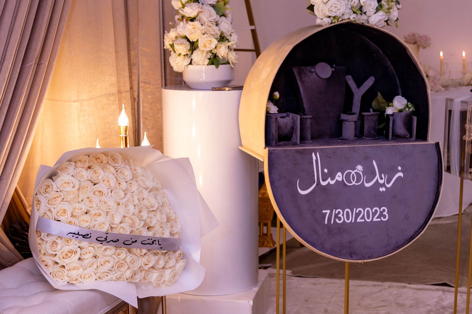 Elegant wedding decor setup with a circular purple sign displaying Arabic text and date 7/30/2023 alongside floral arrangements.