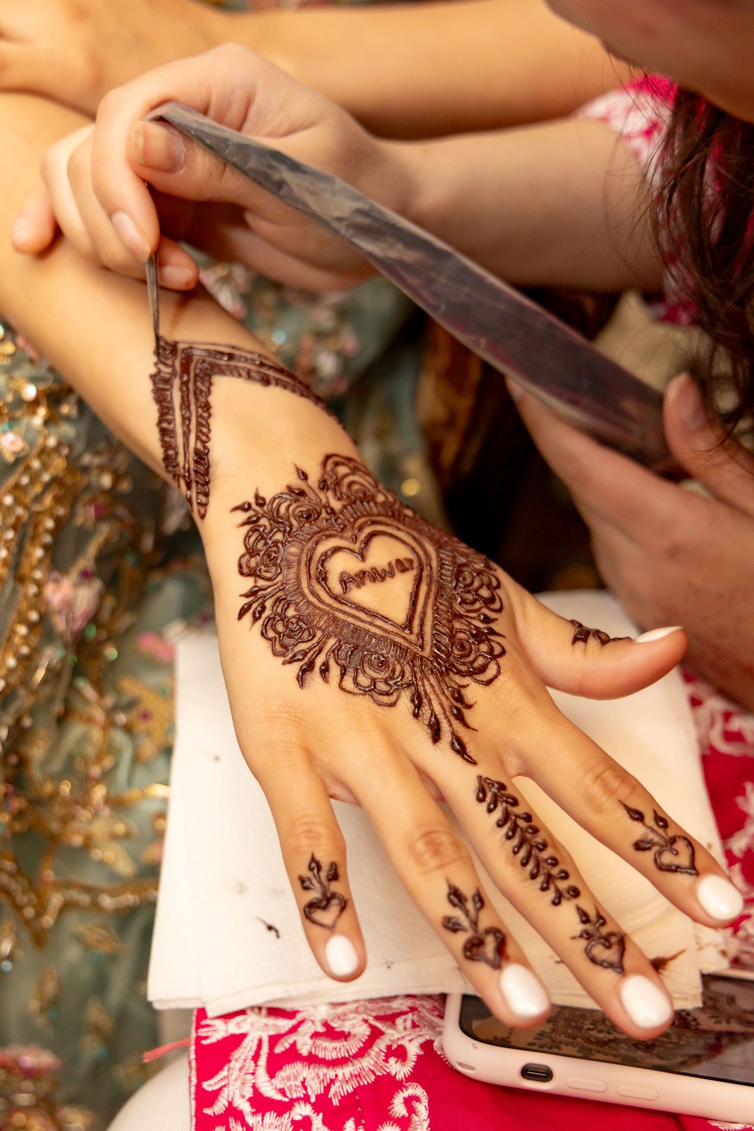 A detailed heart-shaped henna design being applied to a hand with intricate floral patterns and traditional mehndi artwork.