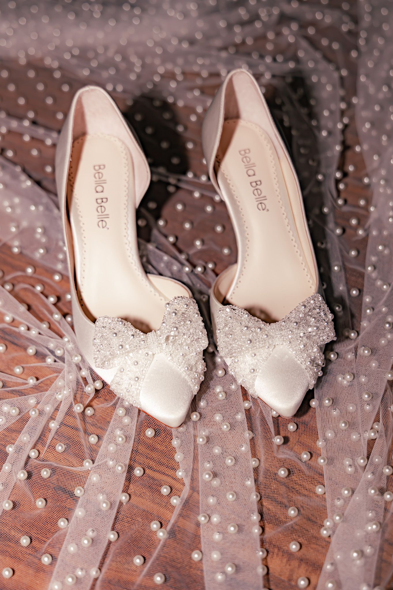 Elegant white bridal shoes with crystal embellishments on polka dot tulle fabric.