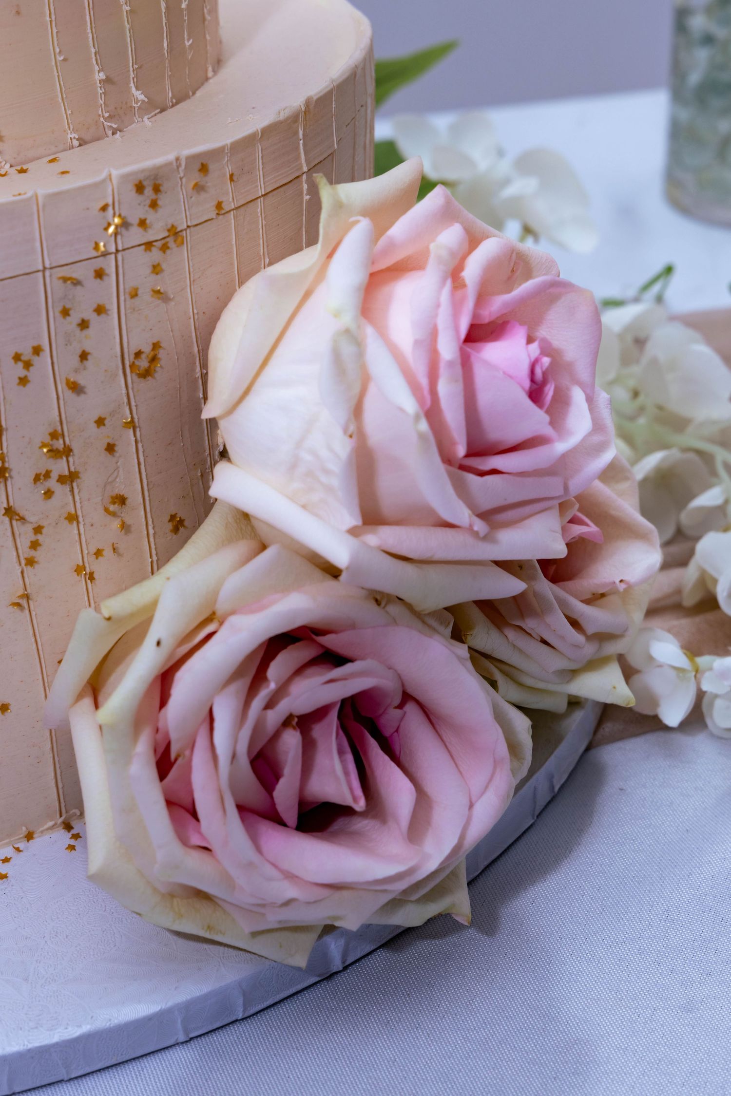 Soft pink roses adorn a cream-colored wedding cake with delicate gold embellishments.