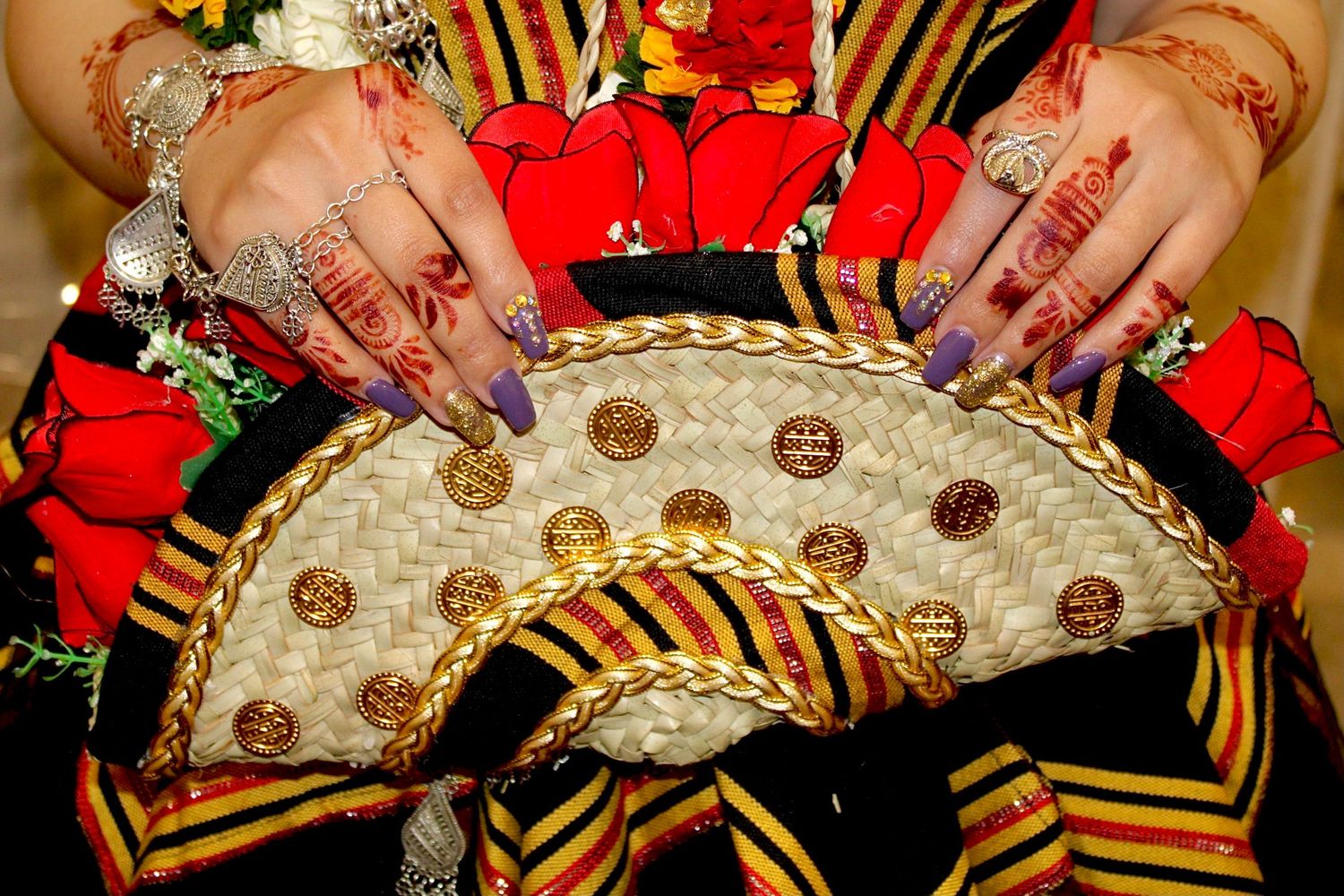 Hands adorned with henna and jewelry showcasing decorative details on a traditional fan with gold buttons.