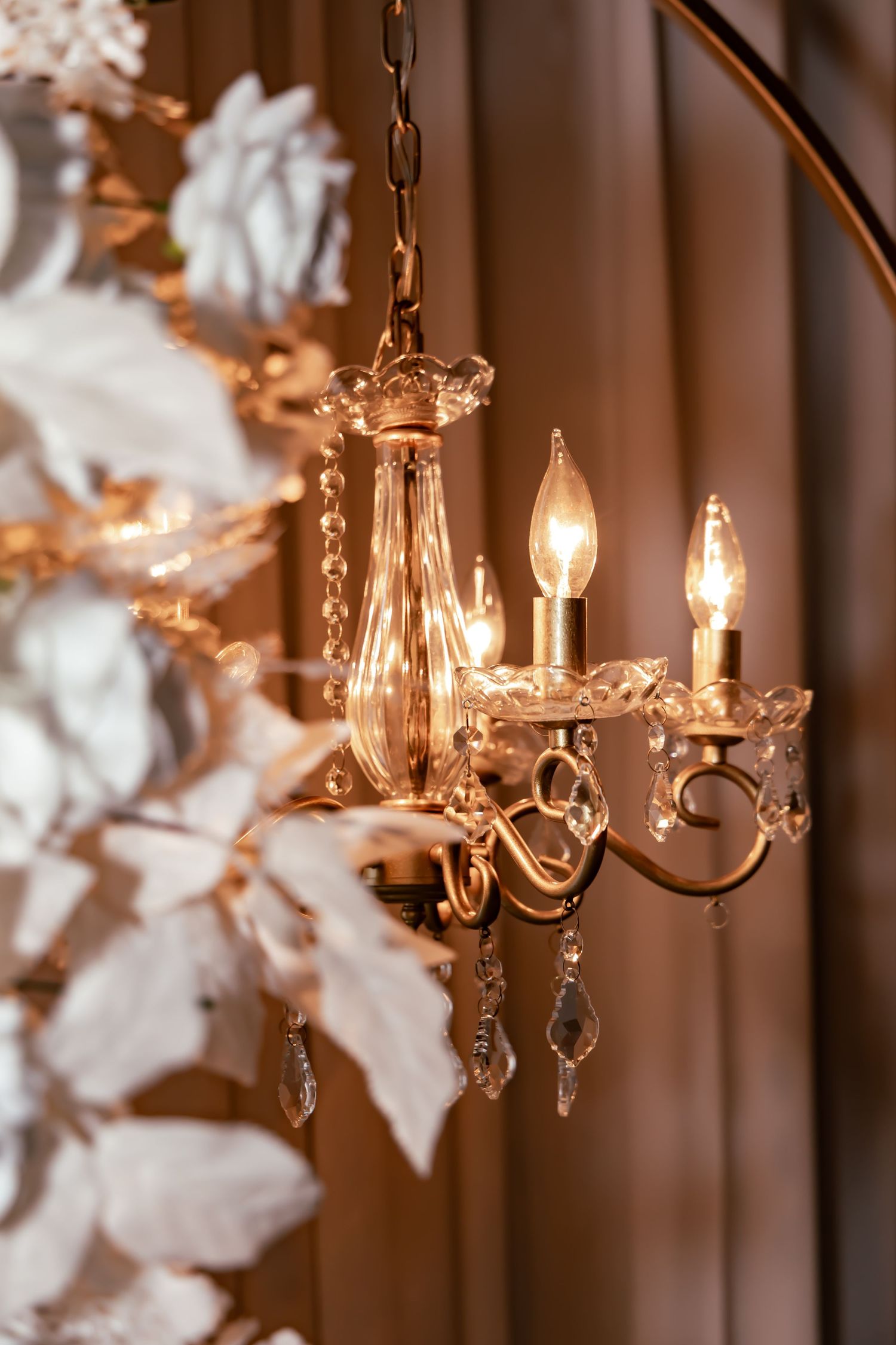 Crystal chandelier with candlelit flames casting warm glow against decorative white flowers.