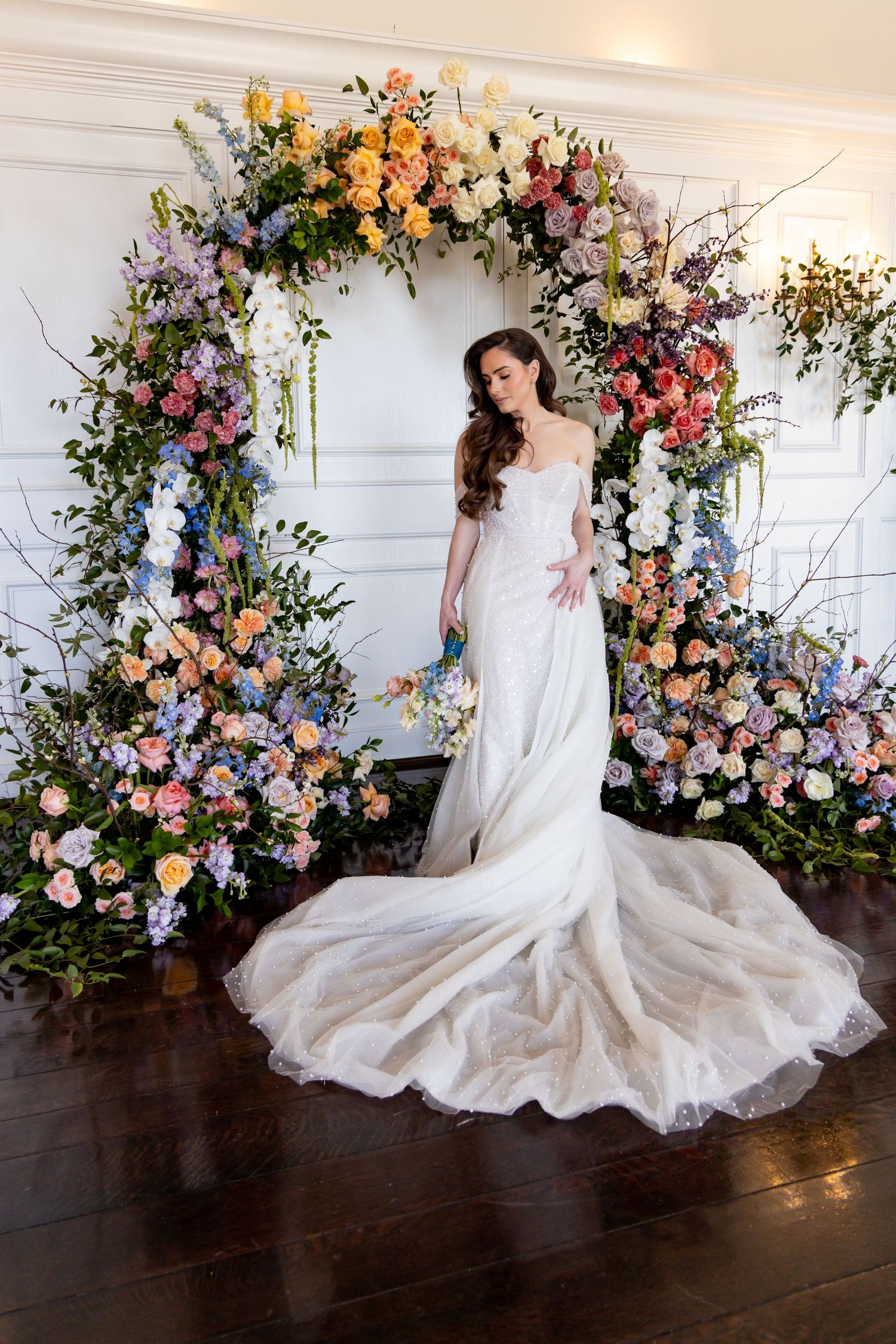 Bride in flowing wedding gown poses under spectacular floral arch installation.