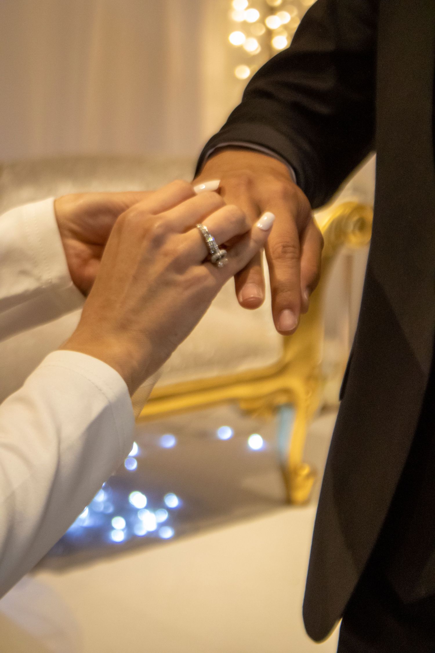Romantic moment of ring exchange between couple with soft lighting and golden frame backdrop.