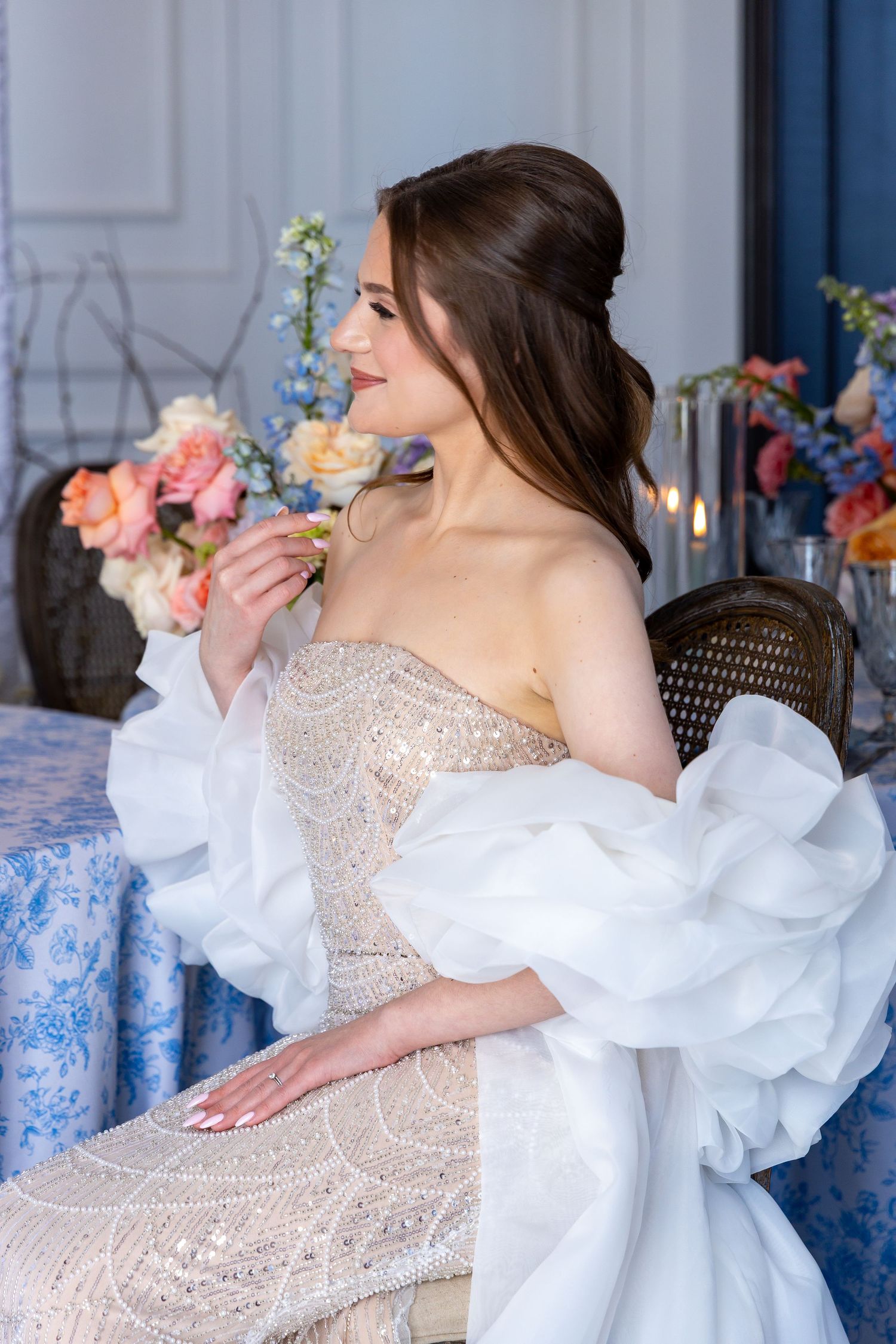 Elegant strapless beaded wedding dress with dramatic white ruffled sleeves and floral table decor in romantic setting.