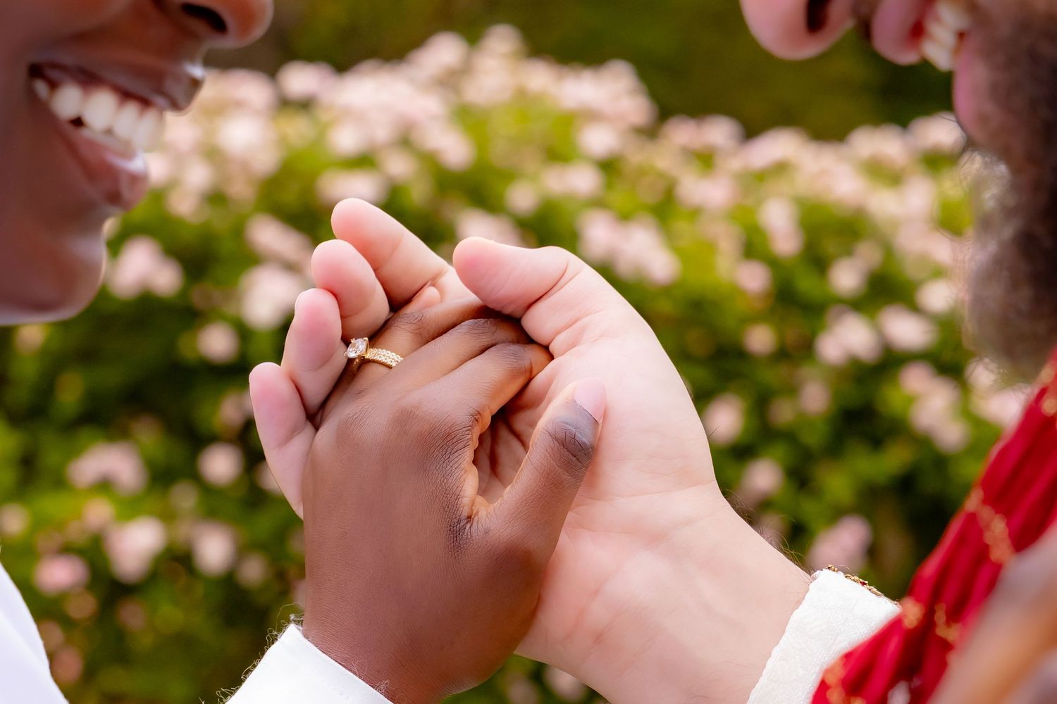 Two hands tenderly clasped together against a soft blurred background of pink spring flowers in bloom. | PHL, PA Wedding Photographer