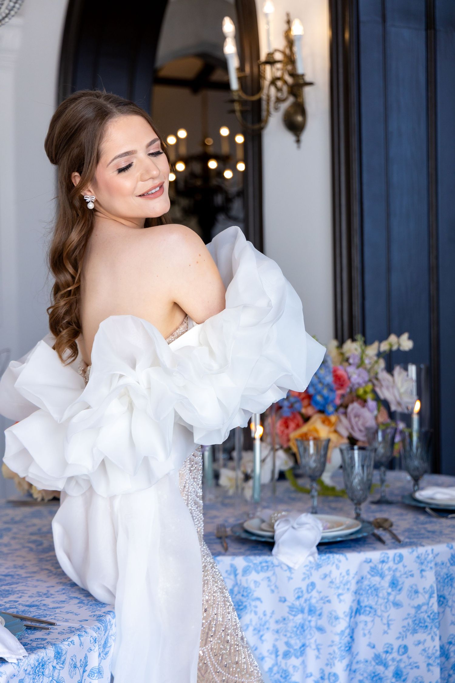 Elegant white wedding dress with dramatic ruffled sleeves and elegant table setting with colorful floral arrangements.