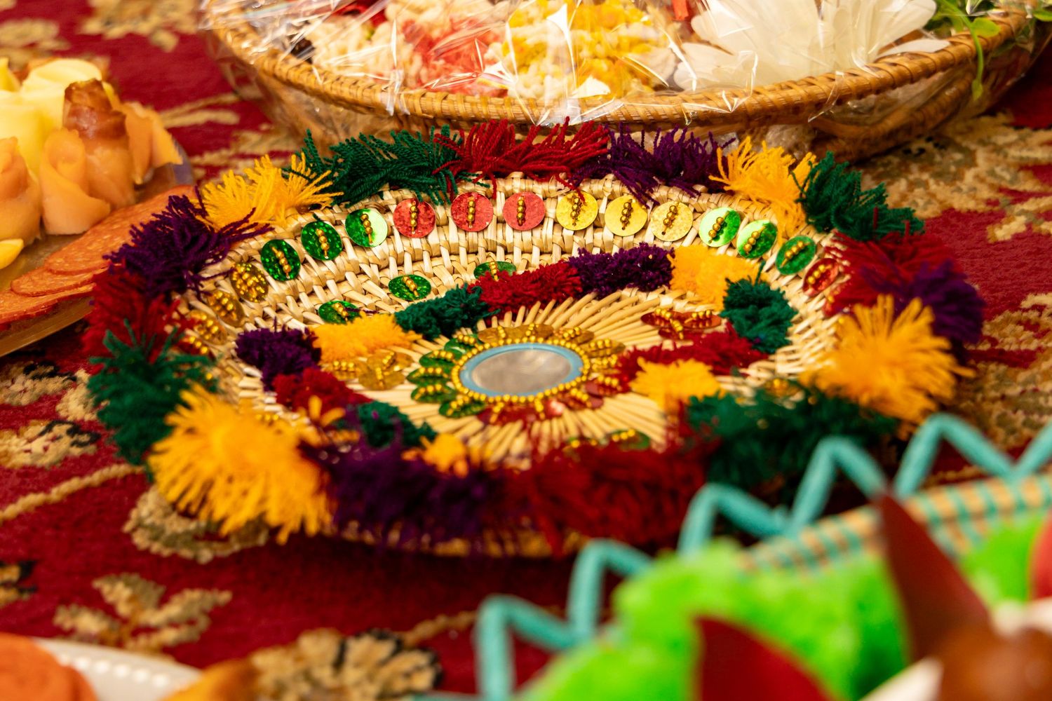 Vibrant floral garland with red, yellow, green and gold decorative elements arranged on burgundy fabric. | PHL, PA Wedding Photographer