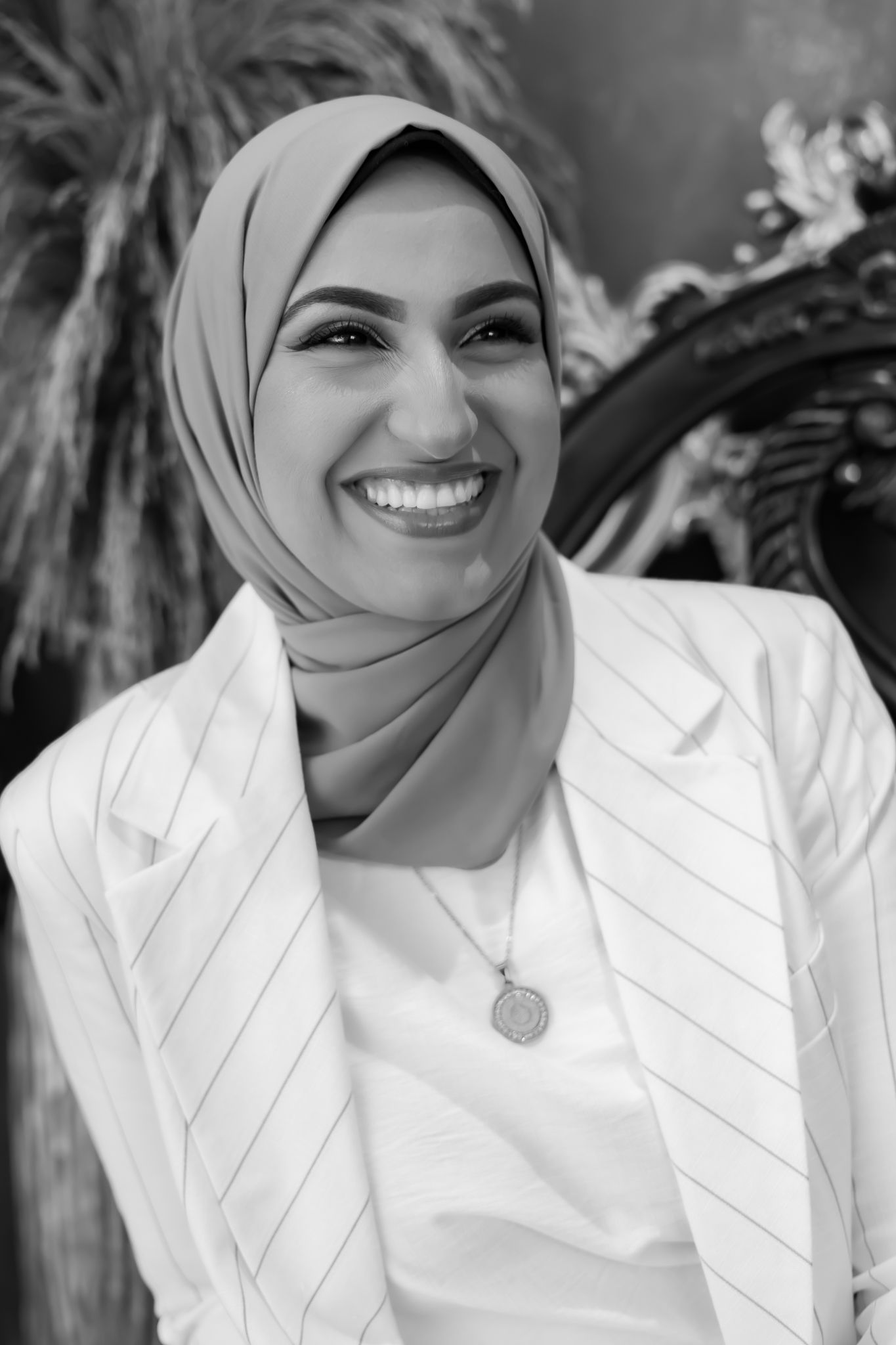Black and white portrait showing someone in a white blazer and hijab wearing a pendant necklace.