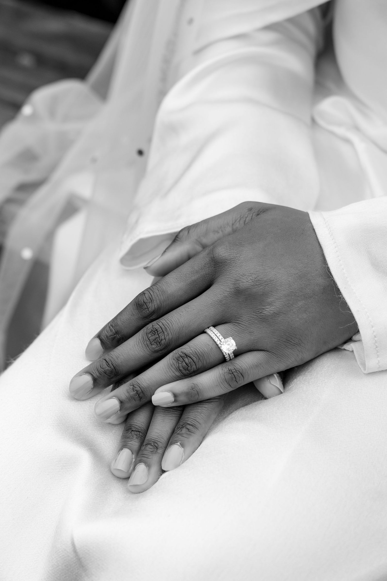 A black and white close-up photo of folded hands wearing a wedding ring against white fabric. | PHL, PA Wedding Photographer | Desi