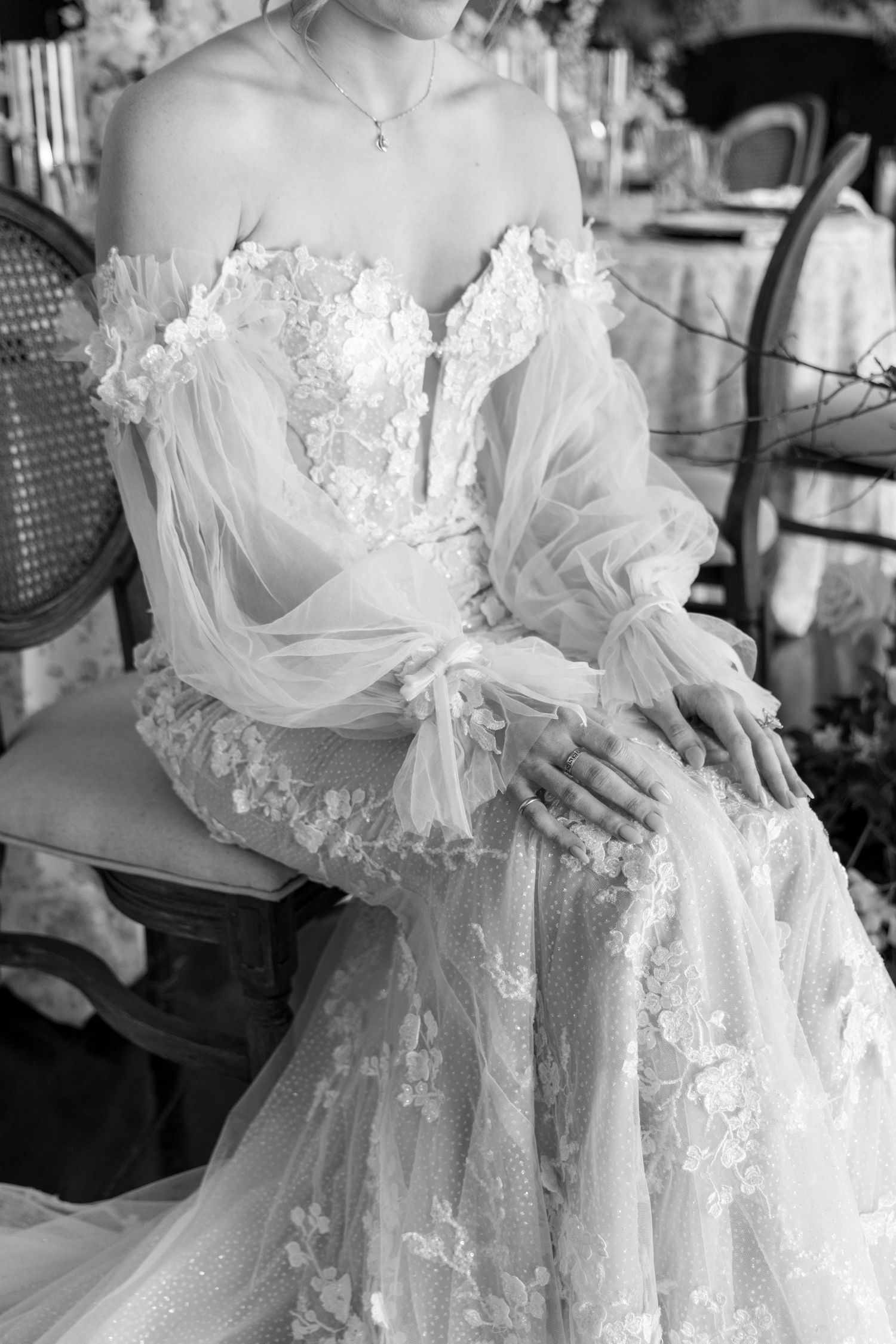 A close-up black and white photo of an ethereal wedding dress with delicate lace details and sheer puff sleeves.