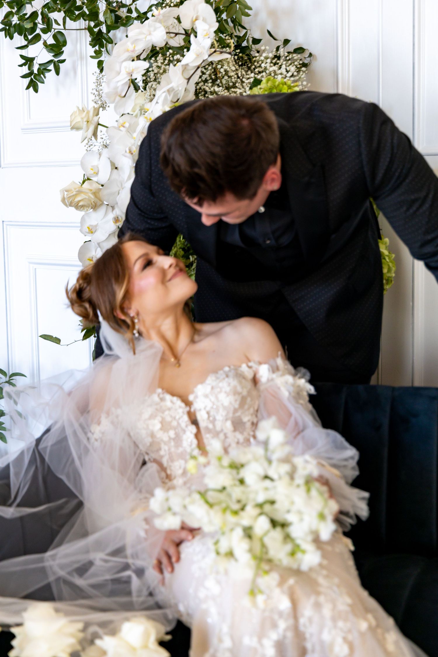 A romantic wedding scene with delicate lace dress details, floral decorations and white bouquet against a light backdrop.
