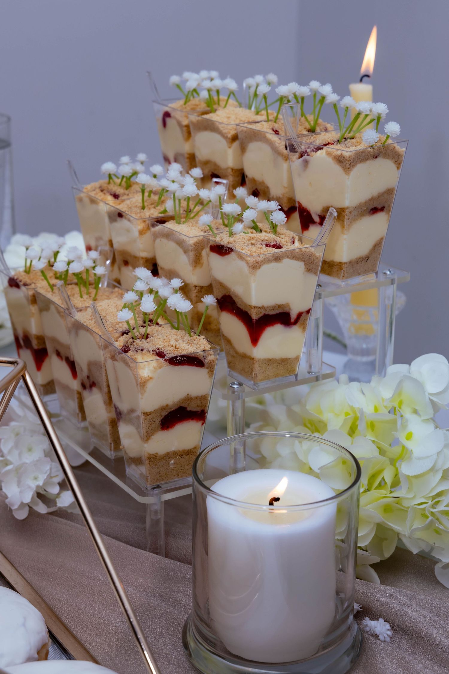 Elegant layered tiramisu desserts in glass cups served with lit candles and white floral decorations on a beige tablecloth.