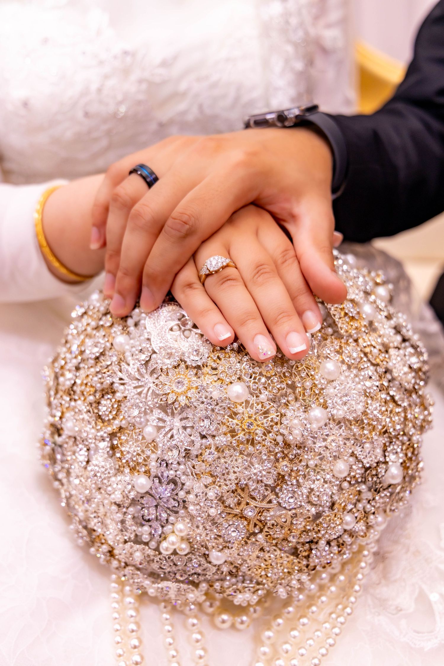 Hands displaying wedding rings on a sparkly crystal-encrusted bouquet holder.